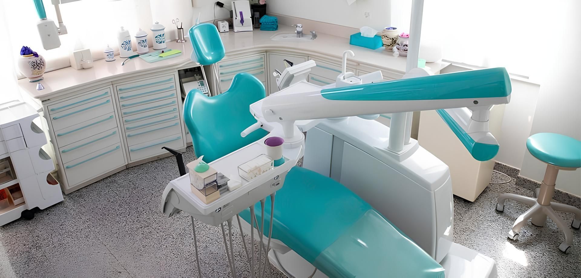 Poltrona odontoiatrica color verde acqua brillante in un moderno studio dentistico bianco con armadietti e attrezzature.