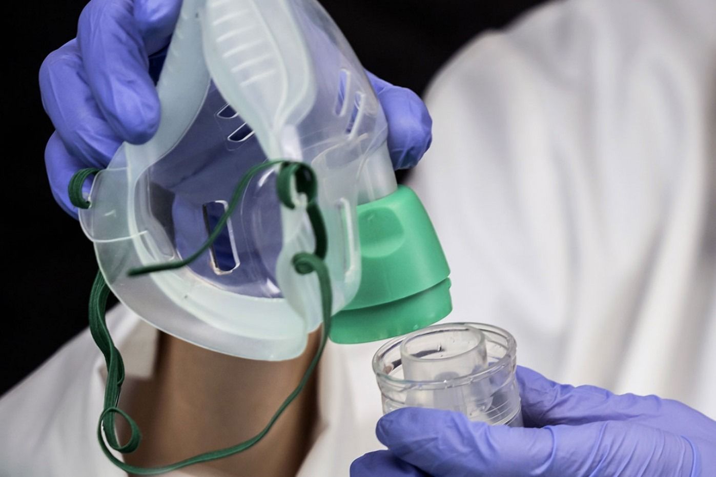 Mani in guanti blu che tengono una maschera per l'ossigeno e un nebulizzatore.