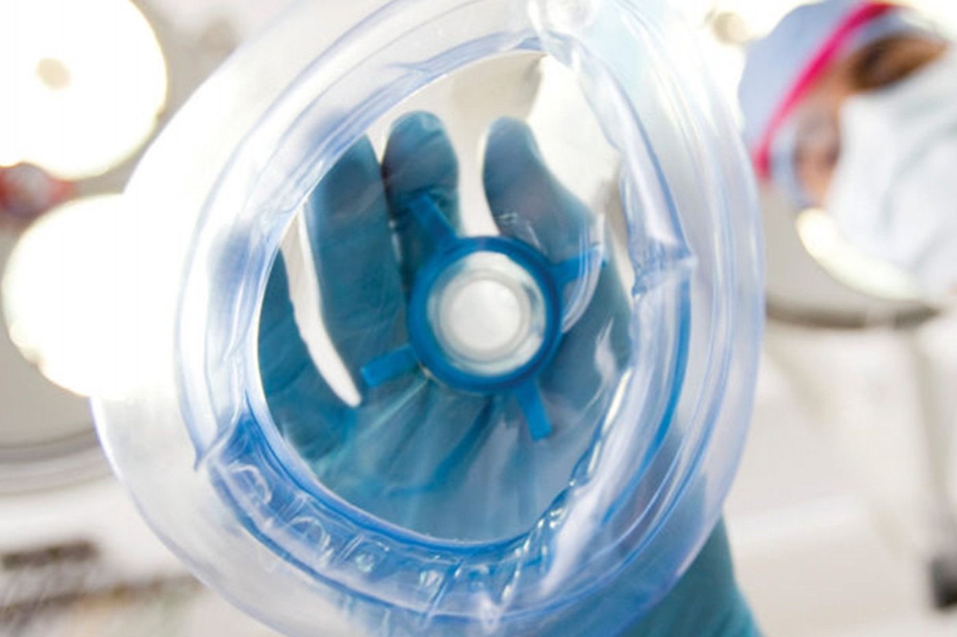 Una persona con guanti blu tiene in mano una maschera per l'ossigeno in una luminosa sala operatoria.