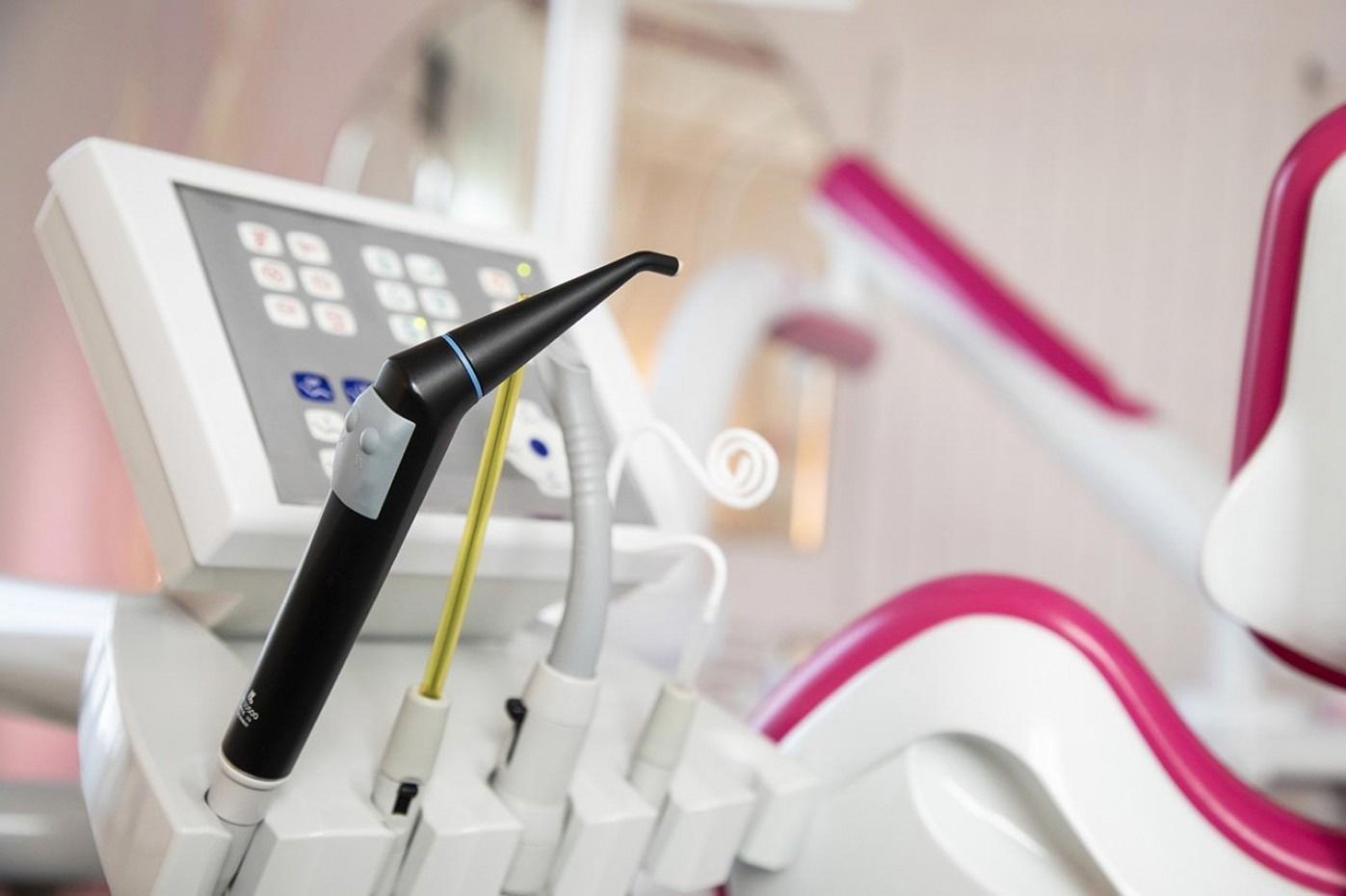 Una poltrona odontoiatrica dal design rosa e bianco, con attrezzatura odontoiatrica e un monitor.