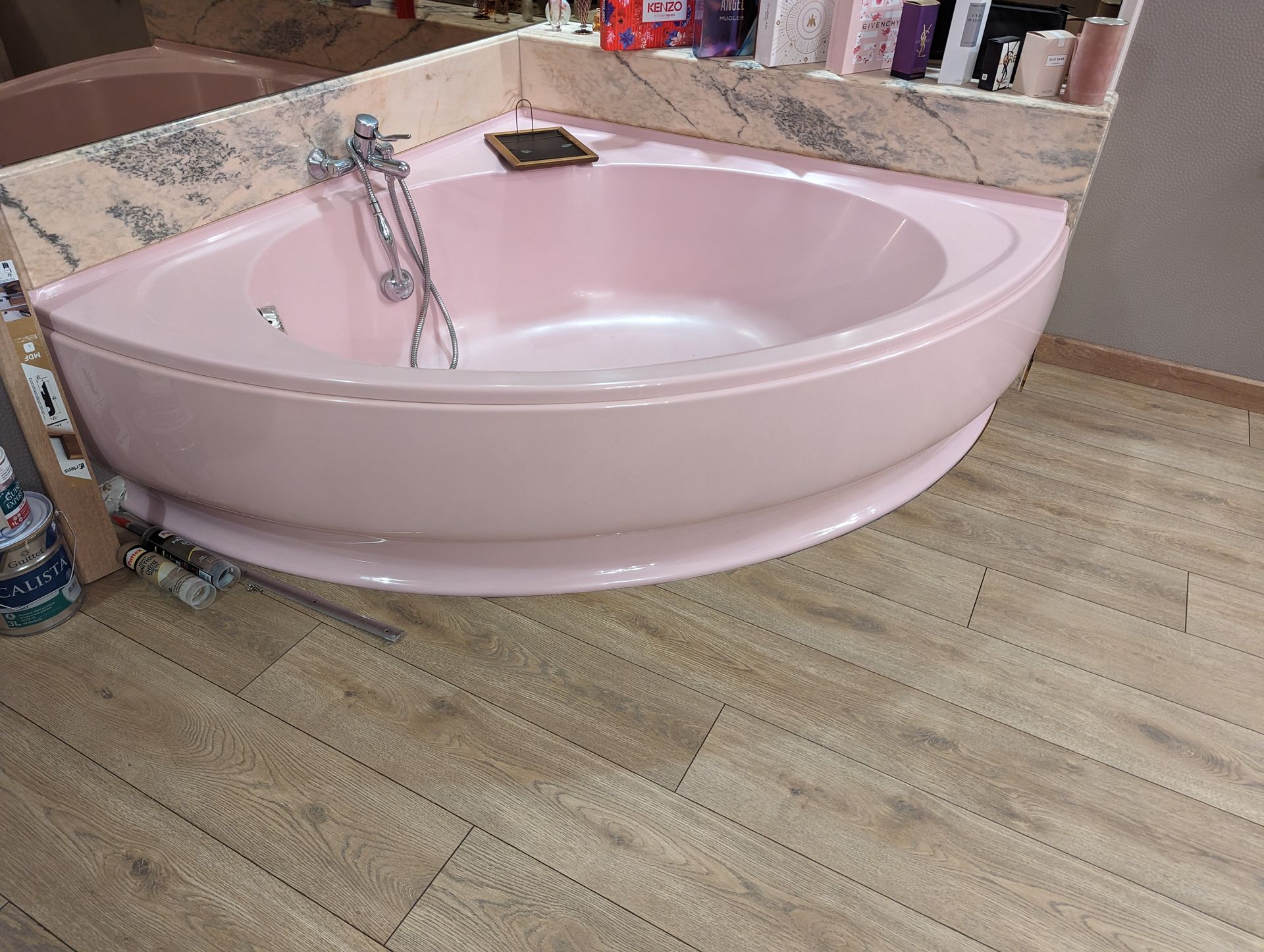 Baignoire d'angle rose dans une salle de bains avec sol imitation bois.
