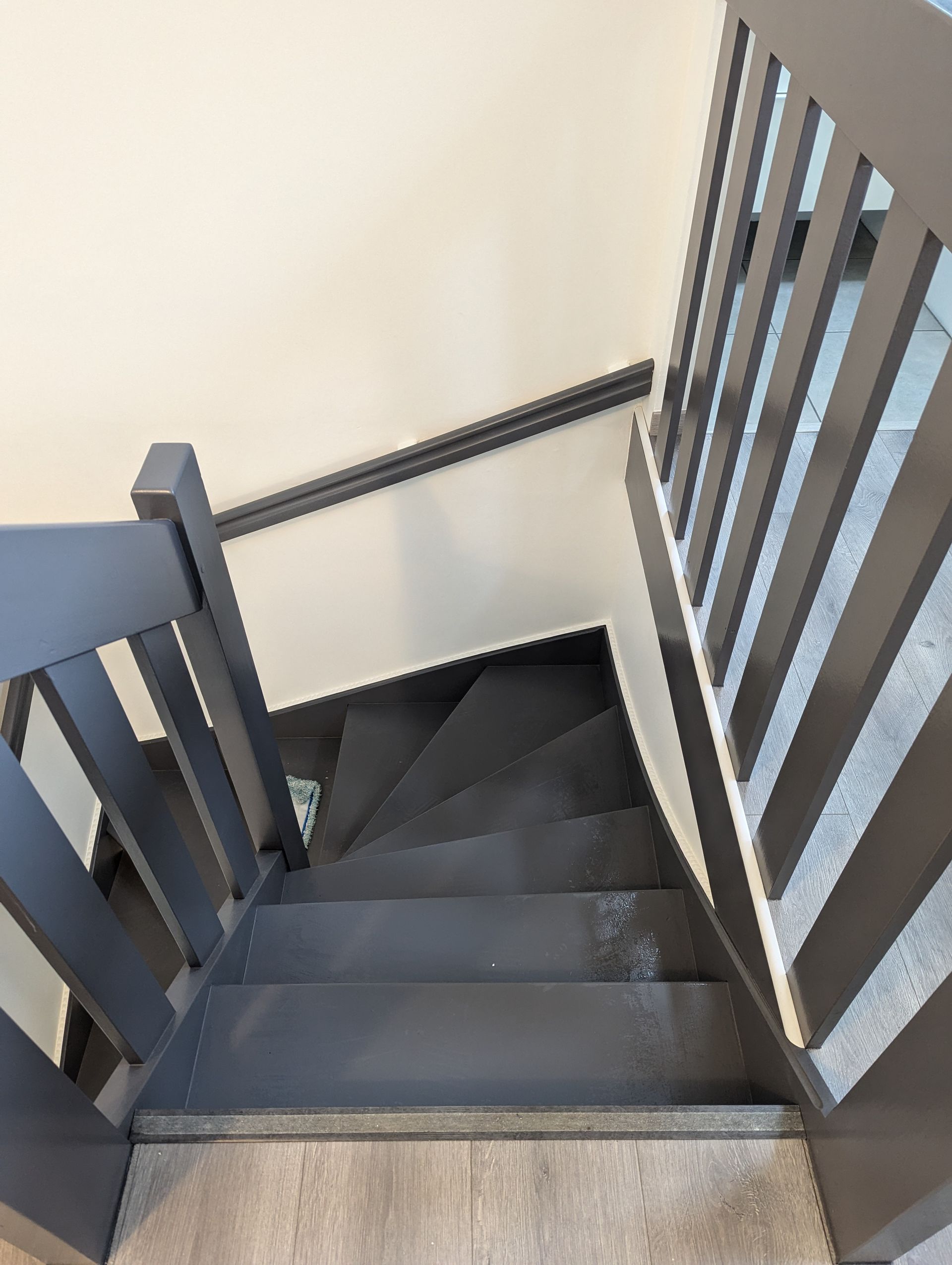 Escalier aux marches et rampes grises, montant contre un mur clair.