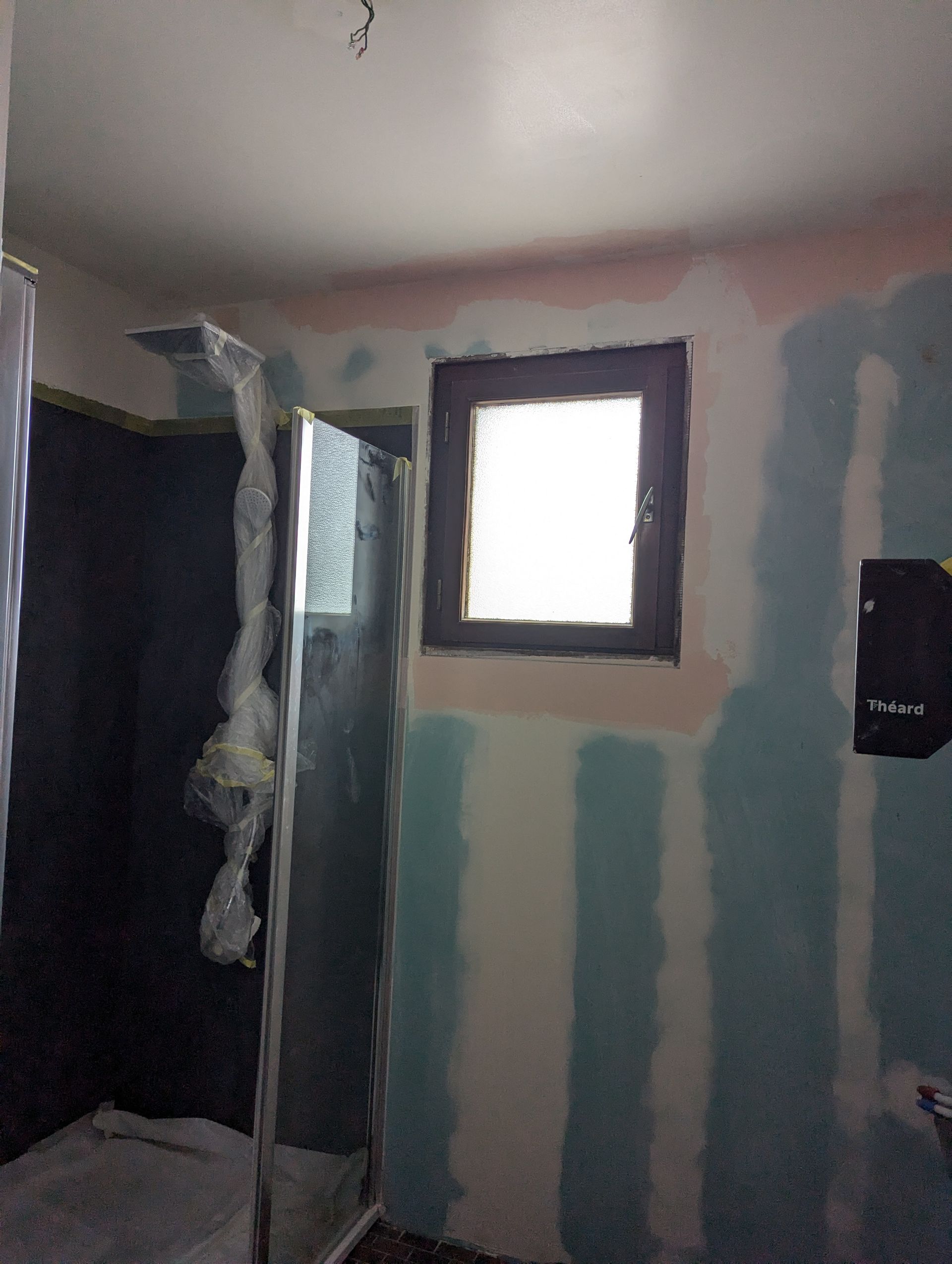 Salle de bains en construction avec douche, fenêtre et cloisons sèches apparentes.