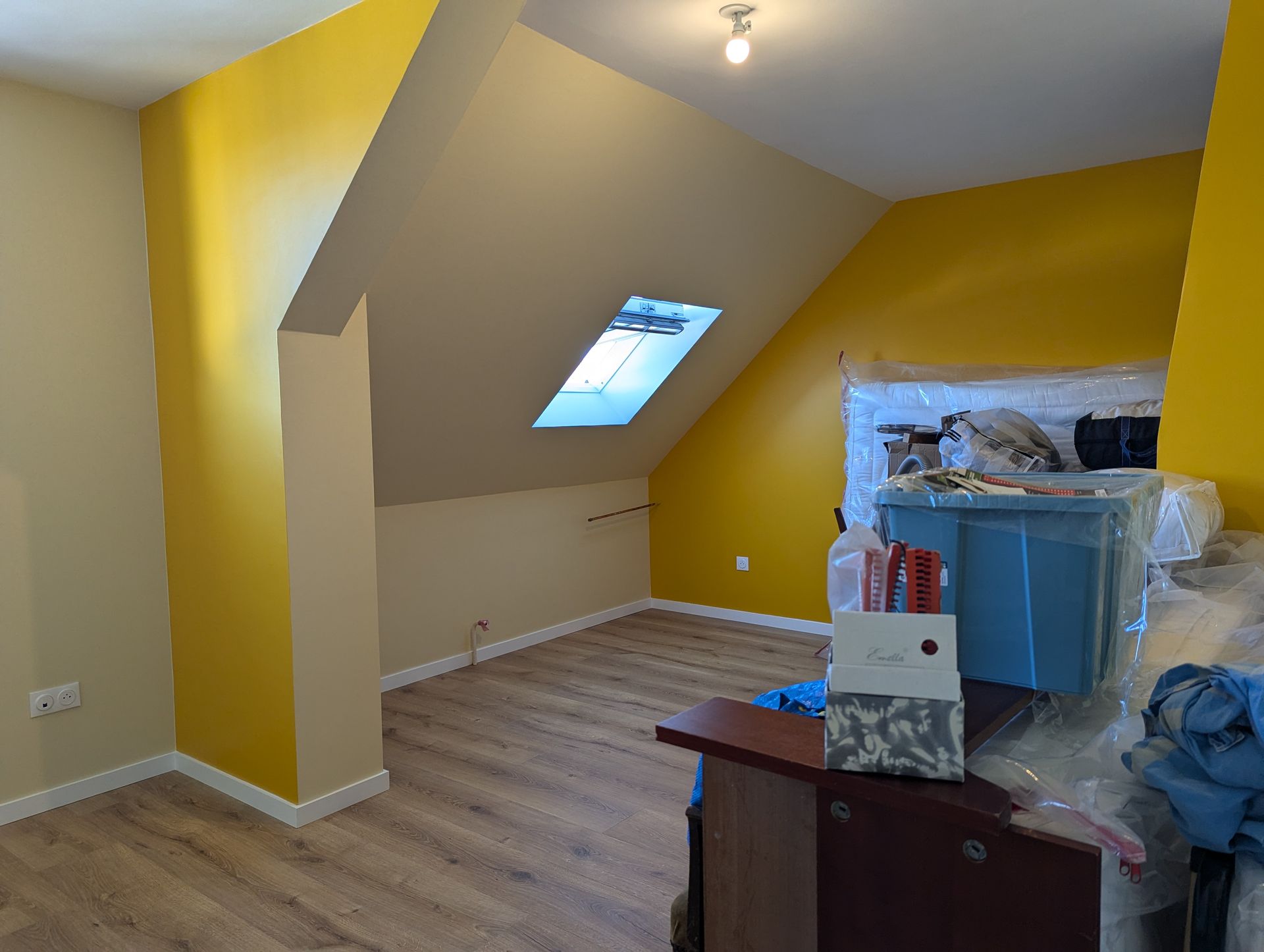 Mur bleu orné d'un tableau coloré au-dessus d'une armoire en bois ; de part et d'autre, des étagères à livres.