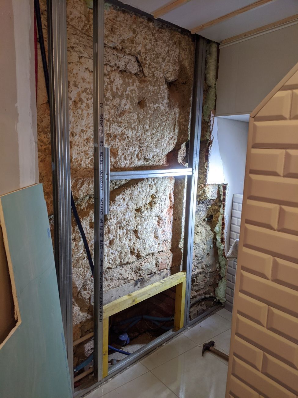 Construction de cloisons intérieures avec montants métalliques, isolation et mur apparent derrière.