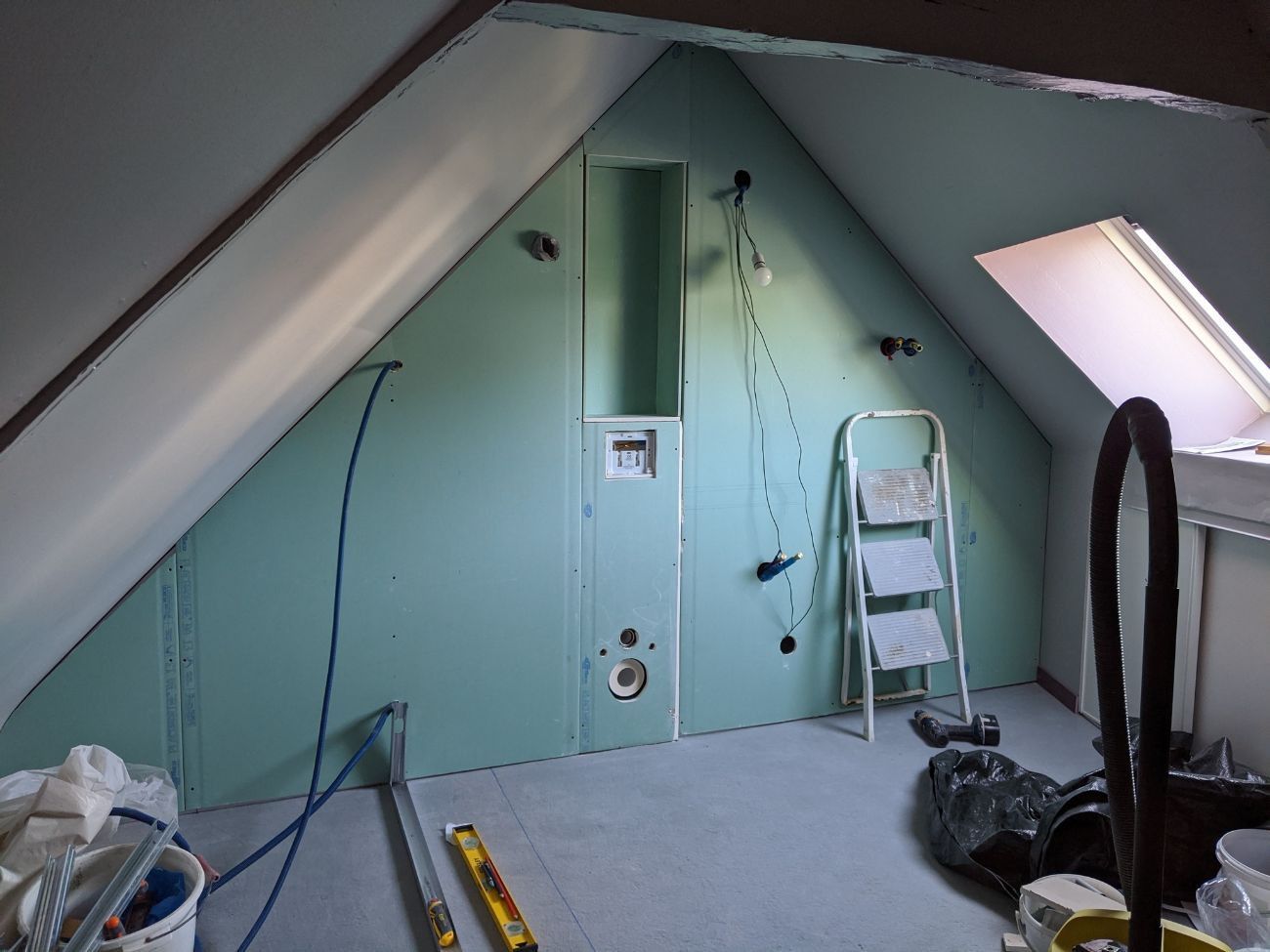 Pièce intérieure aux murs en plaques de plâtre vertes. Plafond mansardé, petite fenêtre.