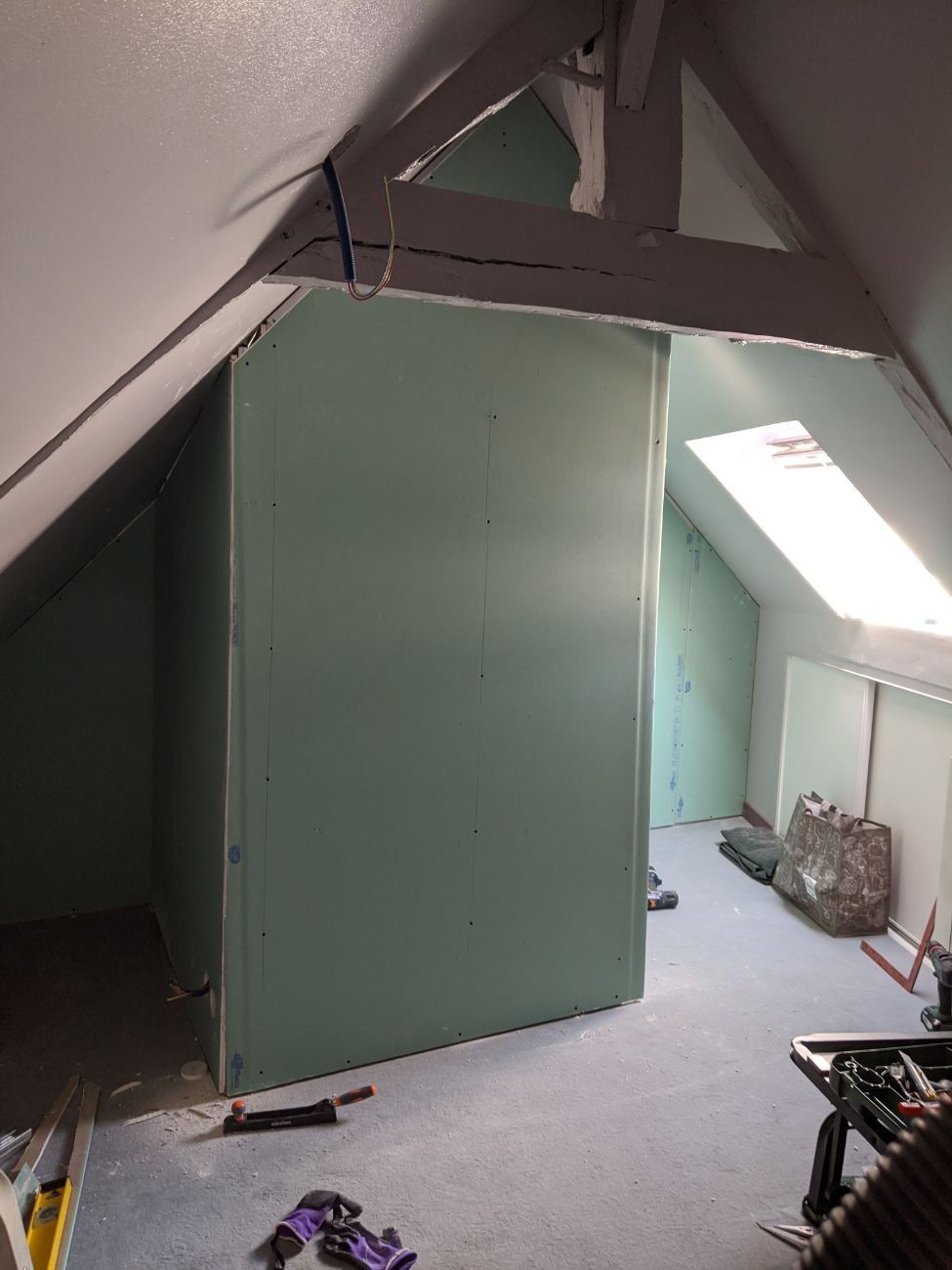 Intérieur du grenier avec une grande cloison vert clair. Plafond mansardé avec puits de lumière.