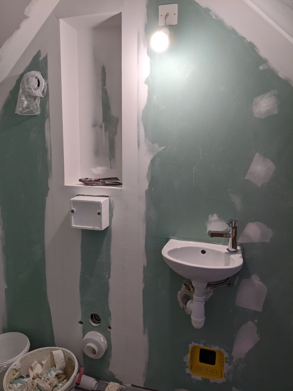Petite salle de bain inachevée avec lavabo, porte-papier toilette et étagère encastrée. Cloisons sèches vertes.