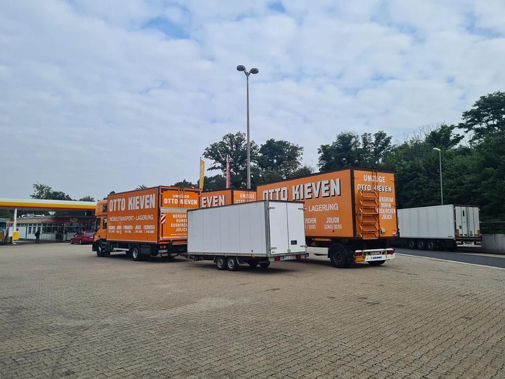 Mehrere Lastwagen stehen auf einem Parkplatz, darunter einer mit der Aufschrift „Otto Hieven“