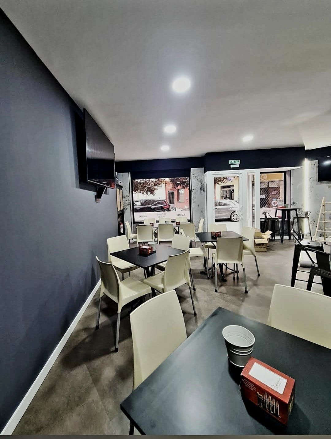 Interior de un café: mesas negras, sillas blancas, pared azul oscuro, entrada abierta a la calle.