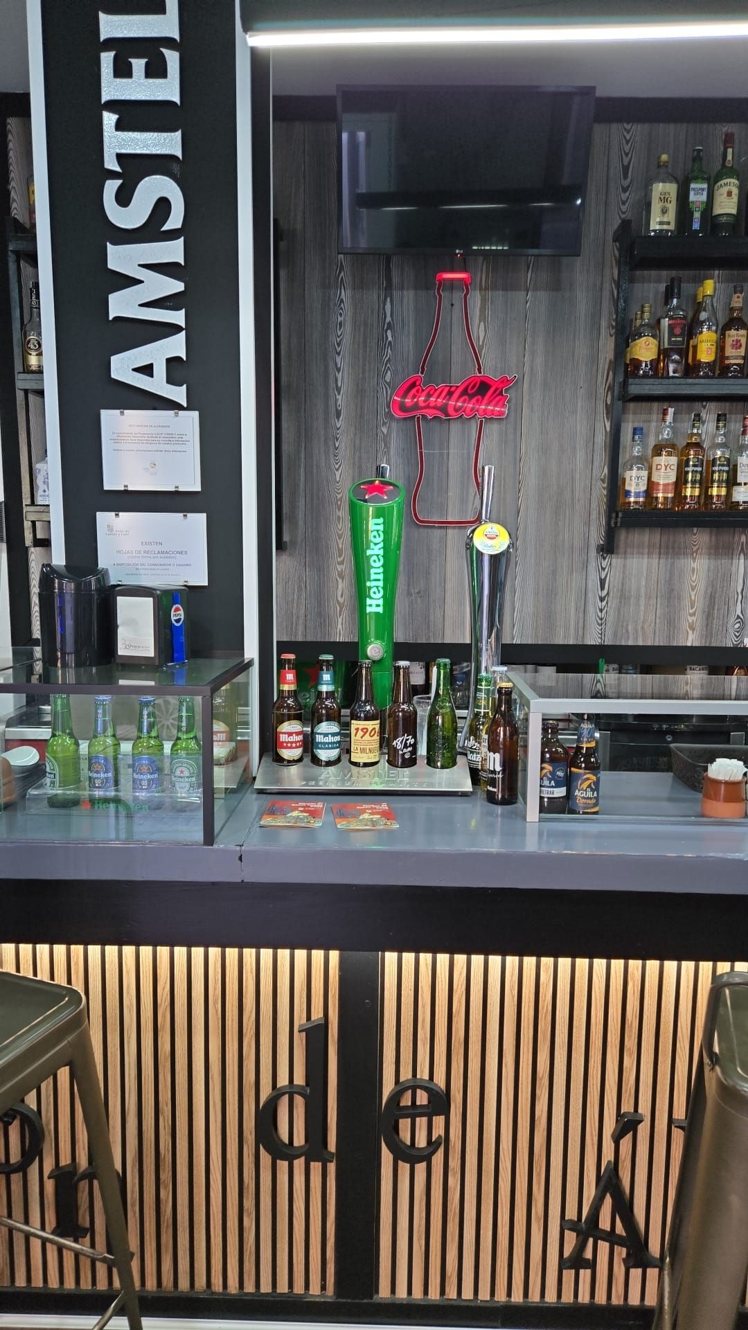 Interior de bar con grifos de cerveza, botellas de licor y un letrero de neón de 