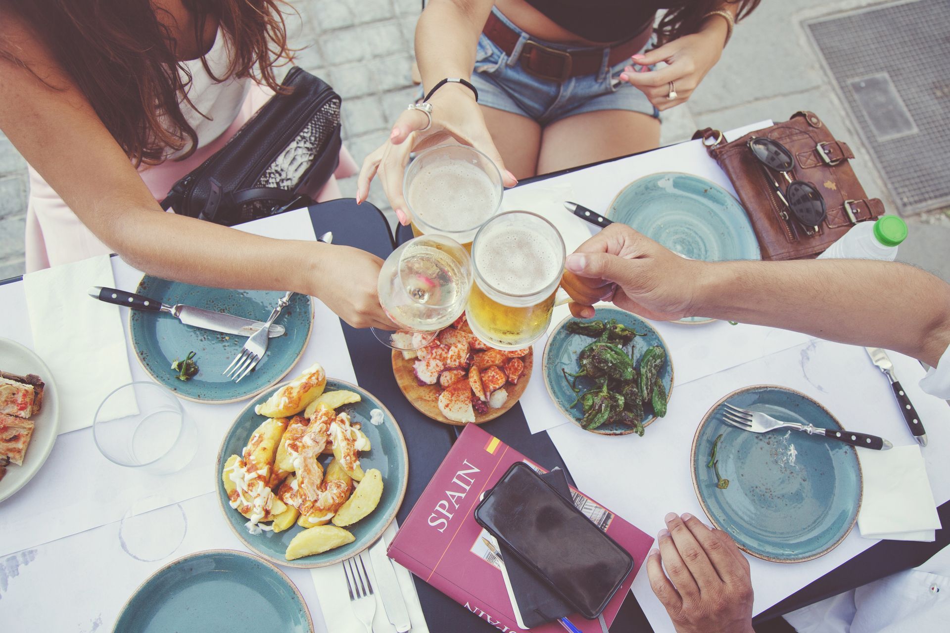 Amigos brindando con cervezas y tapas en una mesa al aire libre en España.