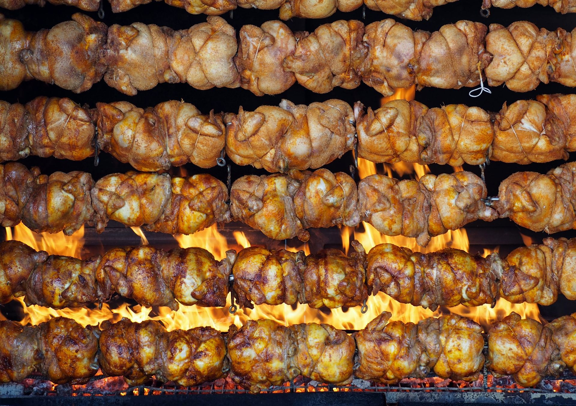 Filas de pollos asados girando sobre las llamas. Aves de corral doradas y cocinadas.