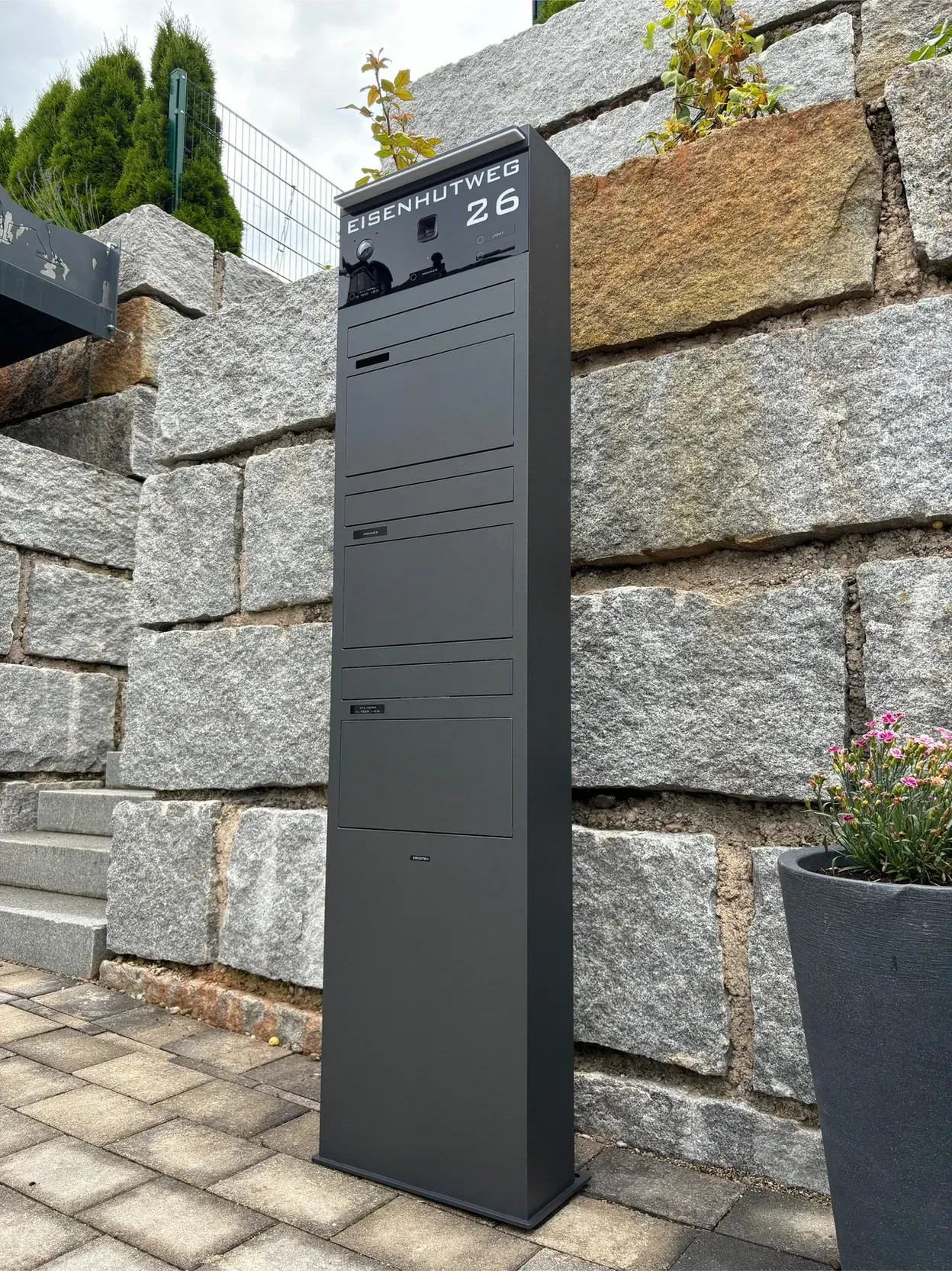 Vor einer Backsteinmauer steht ein schwarzer Briefkasten.