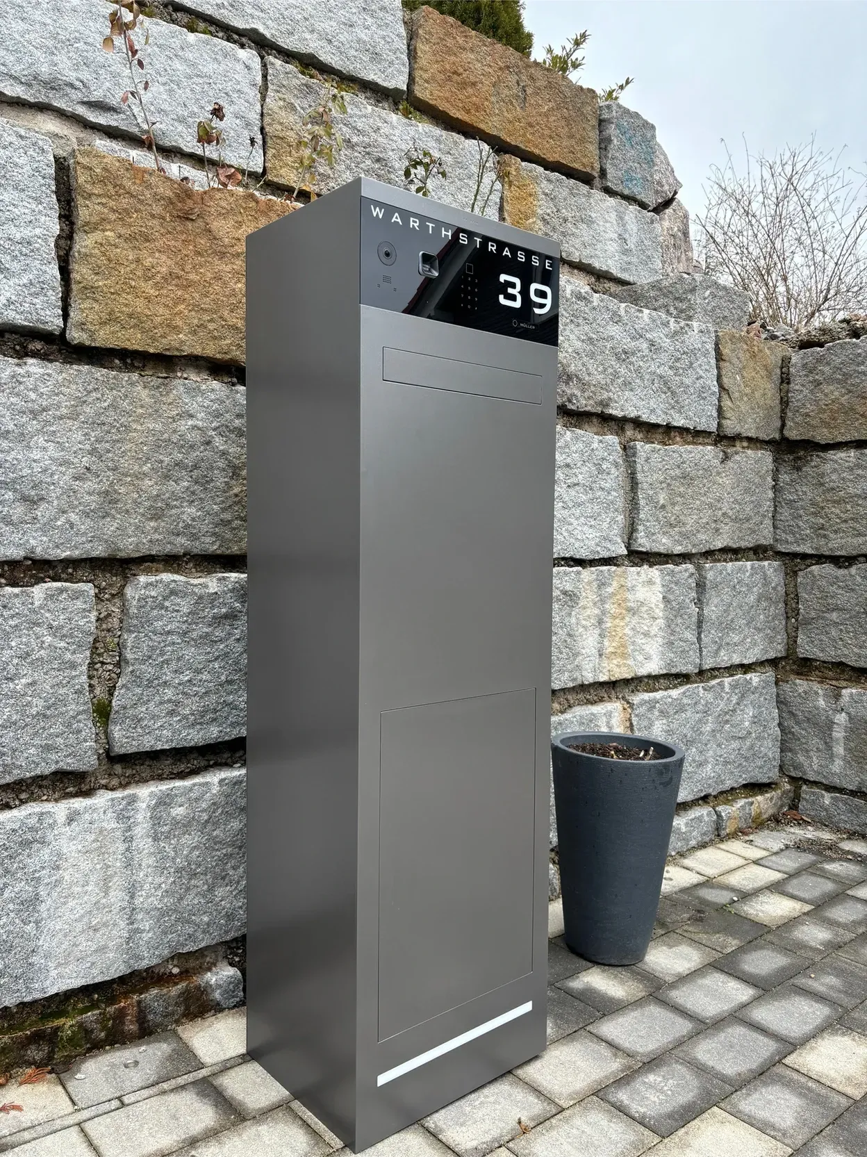Vor einer Backsteinmauer steht ein Briefkasten.