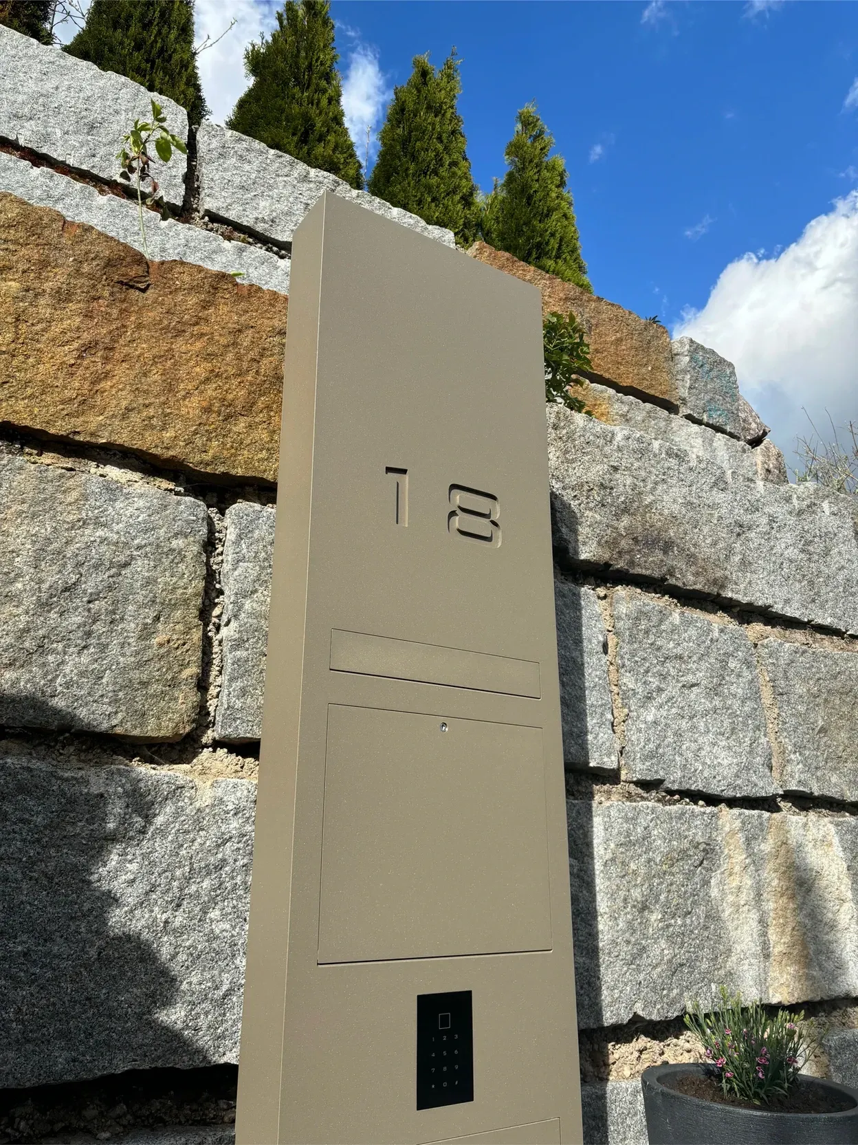 Vor einer Steinmauer steht ein Briefkasten.