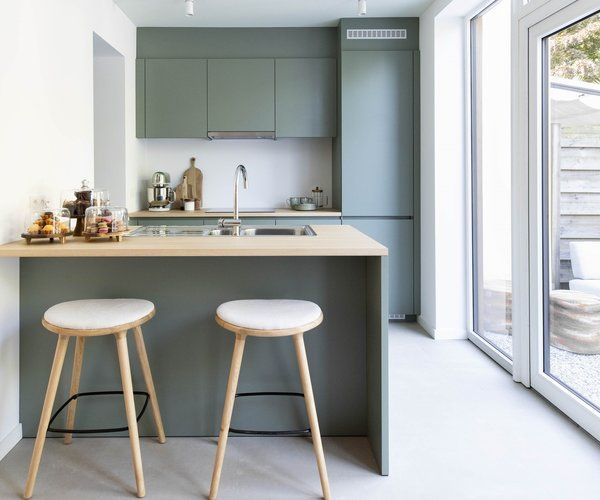 Cuisine vert sauge avec coin repas minimaliste, bar et tabourets en bois clair