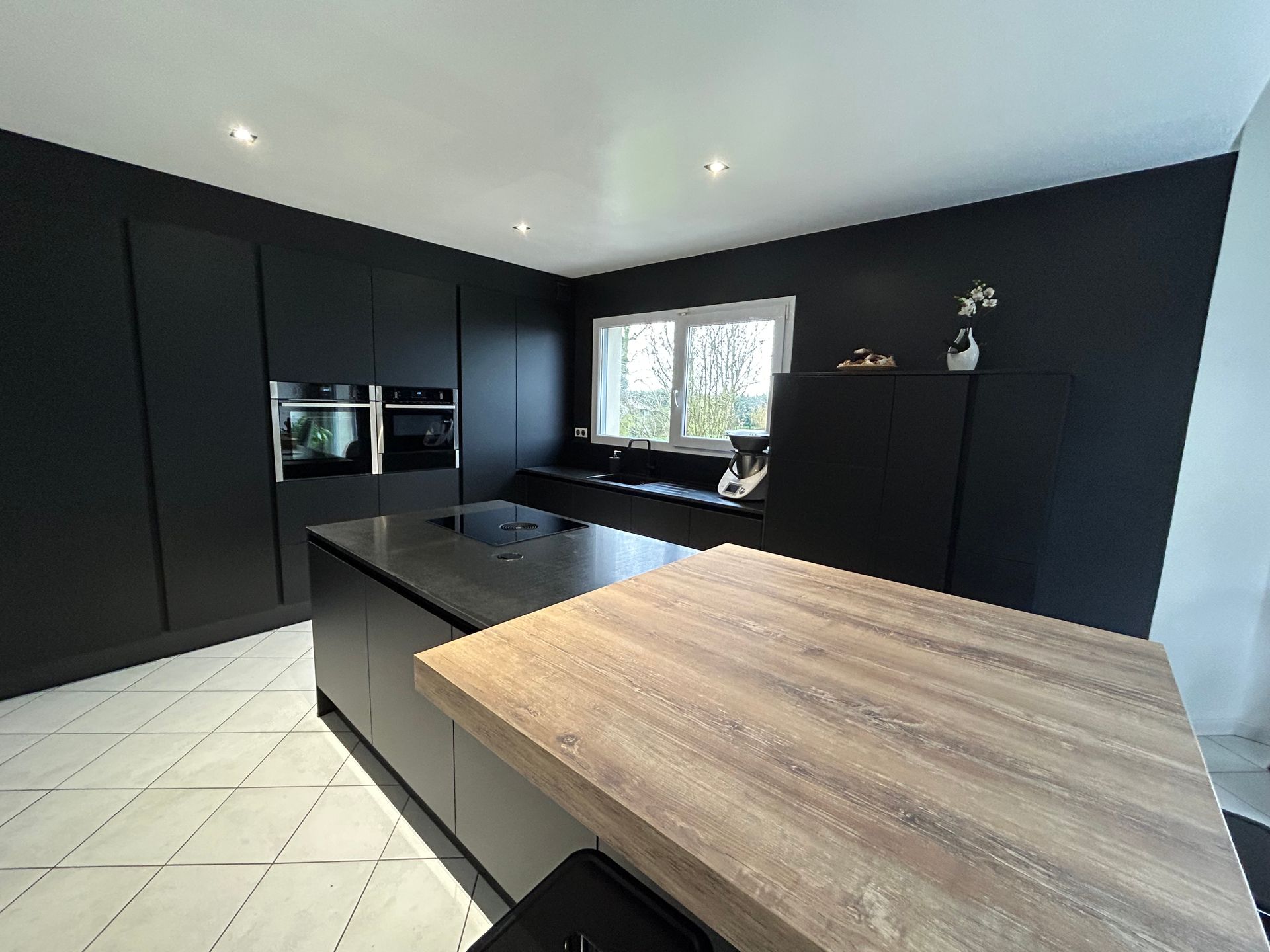 Cuisine ouverte avec meubles noirs mat et coin repas en bois brut