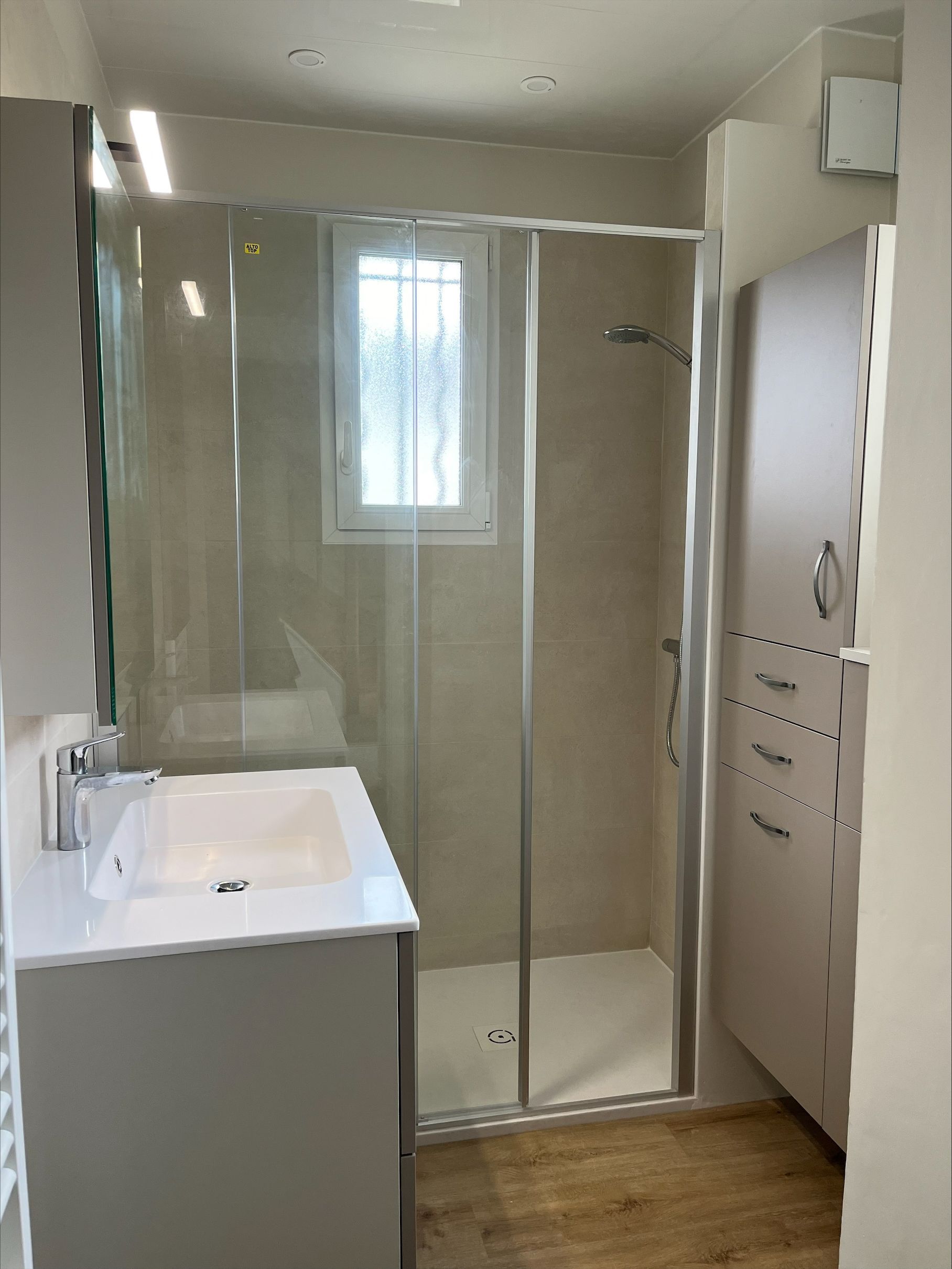 Meuble vasque blanc et douche à l'italienne dans une salle de bains lumineuse