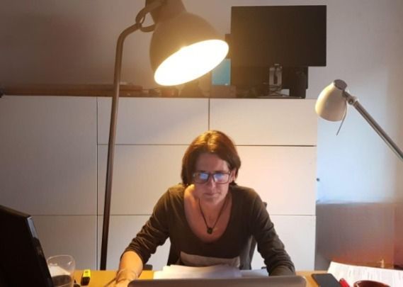 Una mujer con gafas está sentada en un escritorio bajo una lámpara.