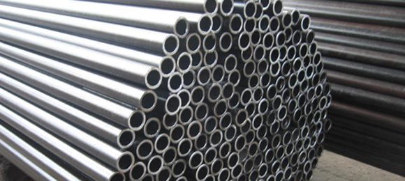 Conjunto de tubos de metal. Cilindros brilhantes, de cor prateada, estão empilhados em um ambiente industrial.