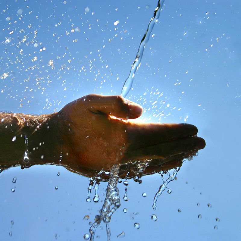 Eine Hand wird vor einem blauen Himmel mit Wasser bespritzt