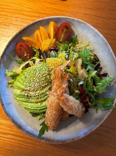 Ensalada con rodajas de aguacate espolvoreadas con semillas de sésamo, camarones fritos y tomates cherry en un plato azul.