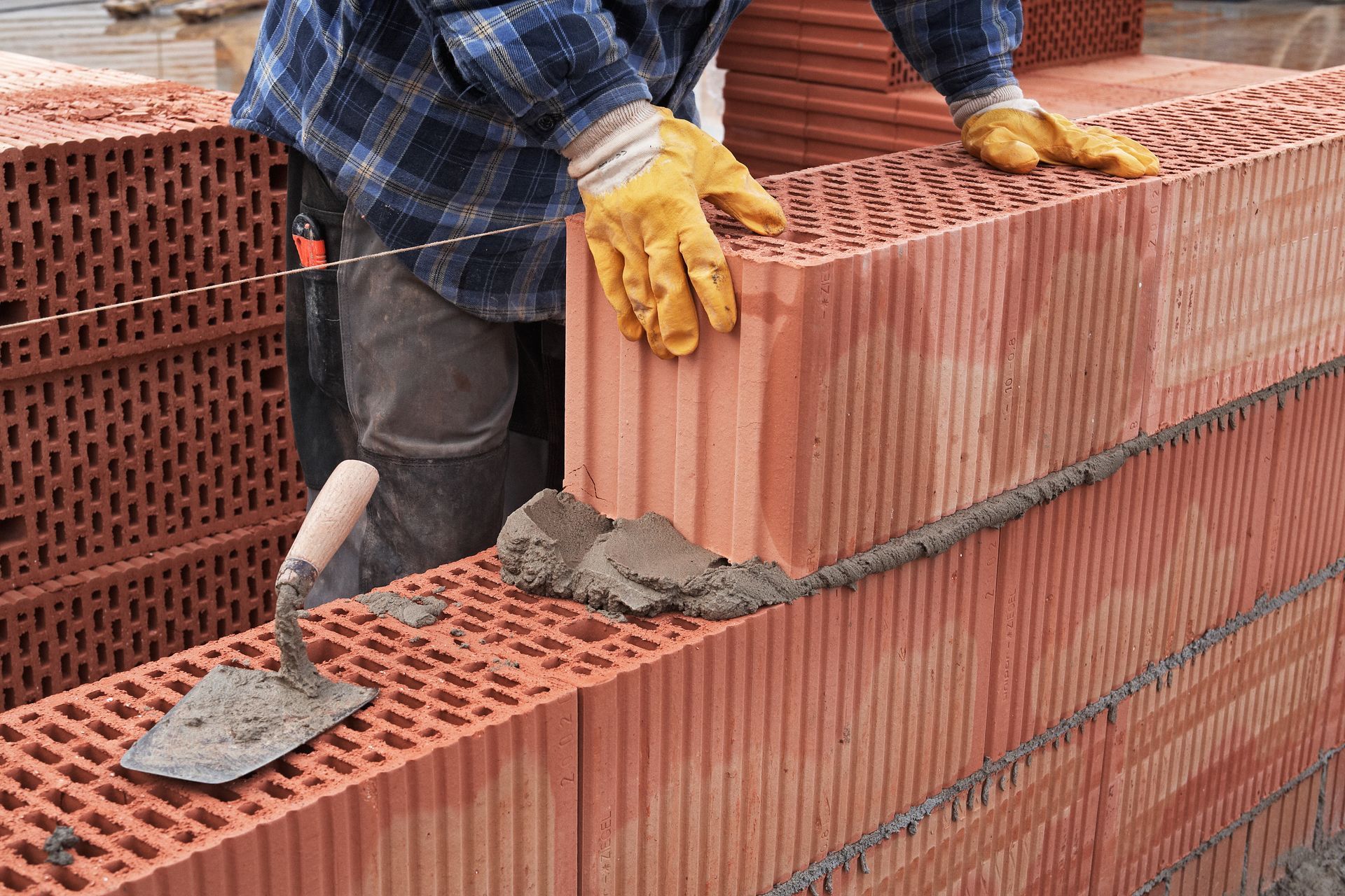 Maurer beim Verlegen einer Ziegelmauer mit Kelle und Handschuhen.