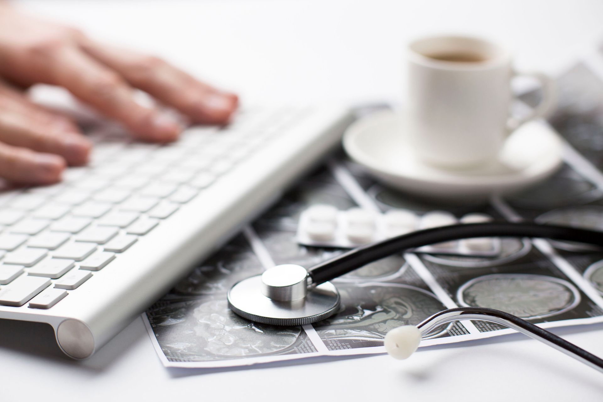 Una persona está escribiendo en un teclado junto a un estetoscopio y una taza de café.