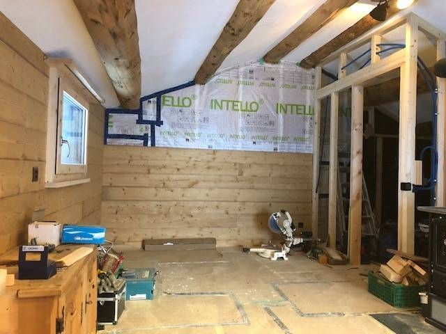 Innenansicht eines im Bau befindlichen Raumes mit Holzbalken, freiliegenden Wänden und herumliegenden Werkzeugen.