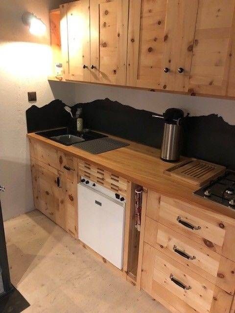 Küchenschränke und Arbeitsplatte aus Holz mit Herd, Spüle und weissen Elektrogeräten; schwarzer Fliesenspiegel.