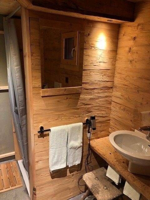 Holzbadezimmer mit Waschbecken, Spiegel und Handtuchhalter; Dusche links sichtbar.