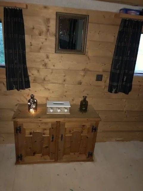 Holzschrank mit Dekoration in einem Zimmer mit Holzvertäfelung, Vorhängen und einem Spiegel.