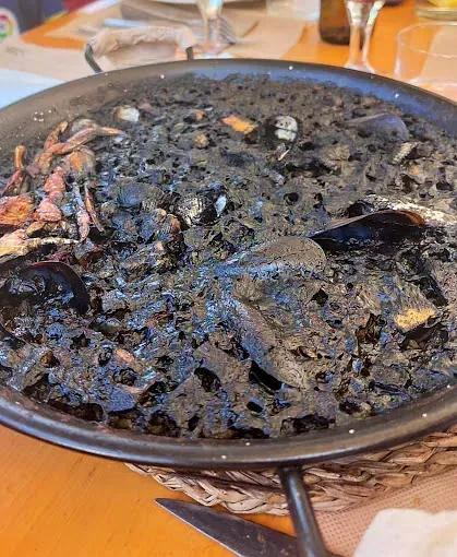 Una sartén llena de arroz negro y mariscos está sobre una mesa de madera.