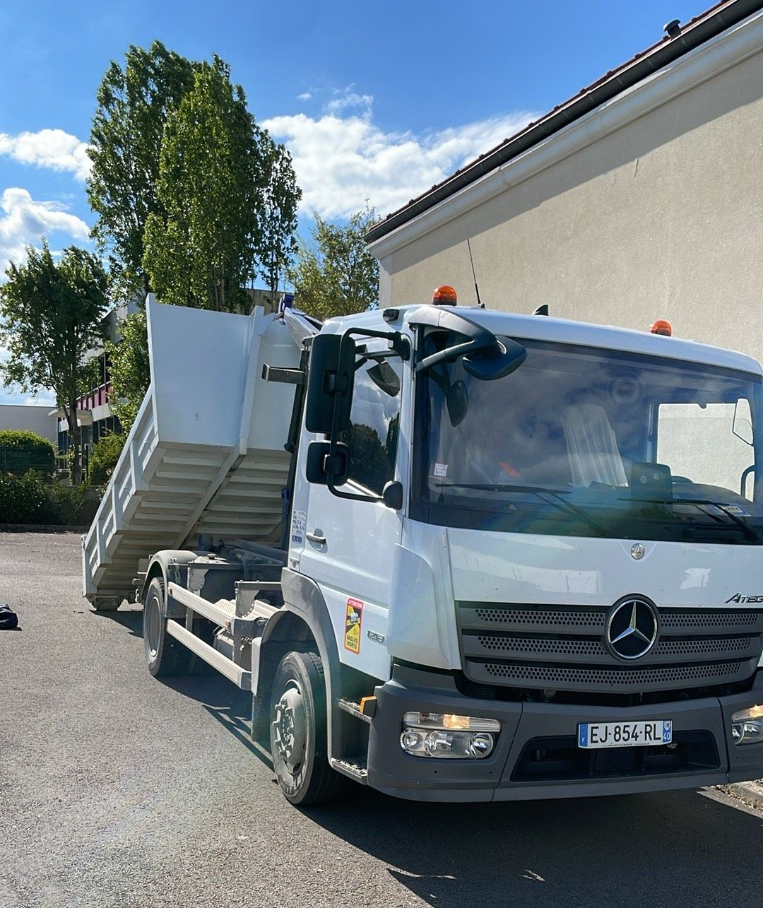 Un camion-benne blanc est garé à côté d'un bâtiment par une journée ensoleillée.