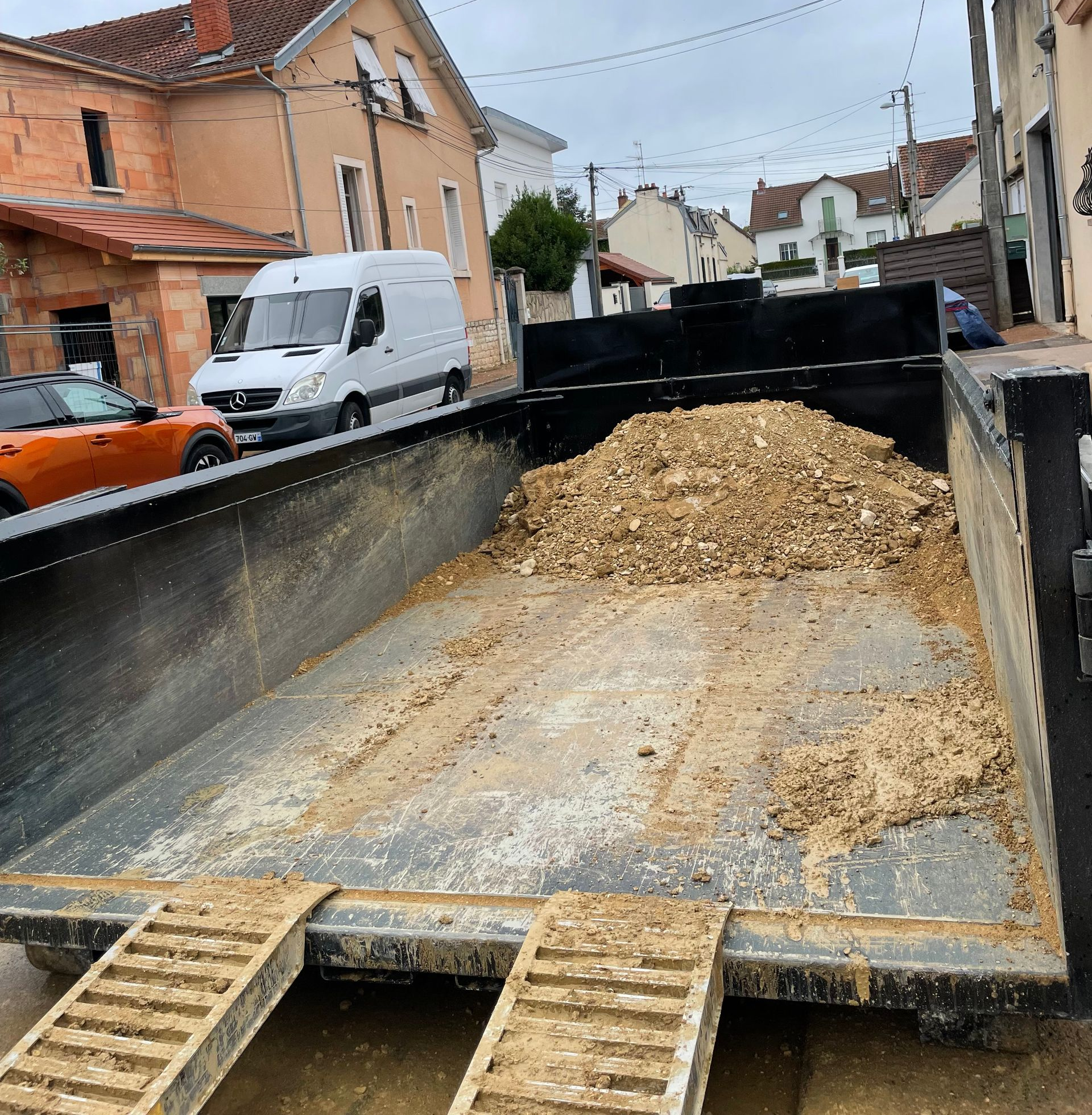 Benne d'un camion remplie de copeaux de bois dans une rue, deux rampes visibles.