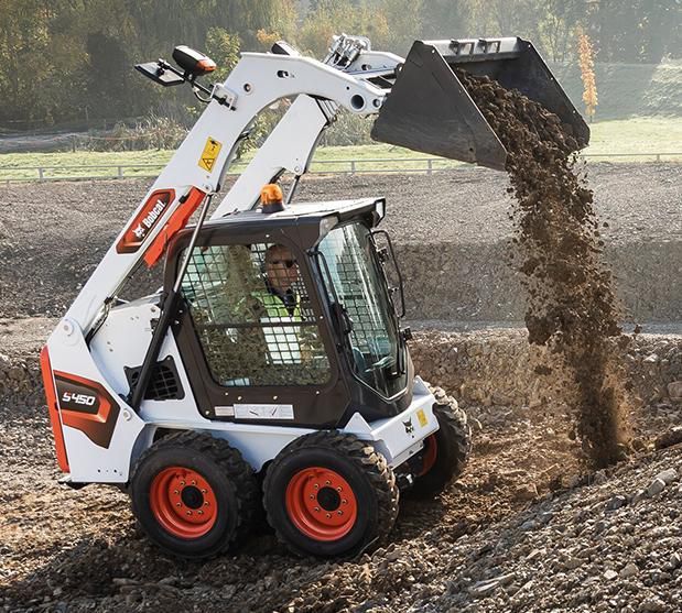 Chargeuse compacte Bobcat déversant de la terre ; opérateur dans la cabine, travaillant à l'extérieur.