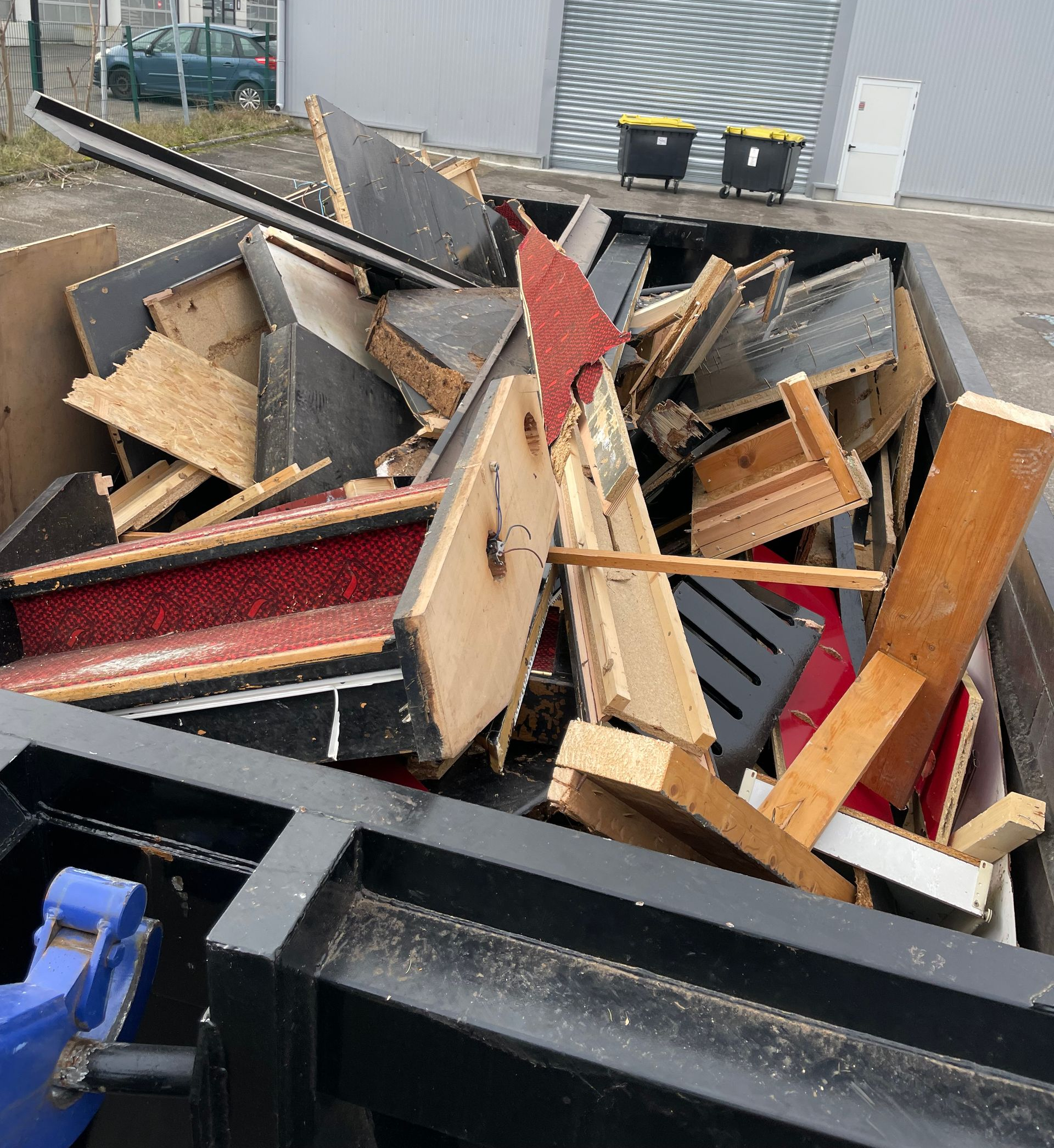 Un tas de meubles démontés et de chutes de bois dans une benne à ordures.