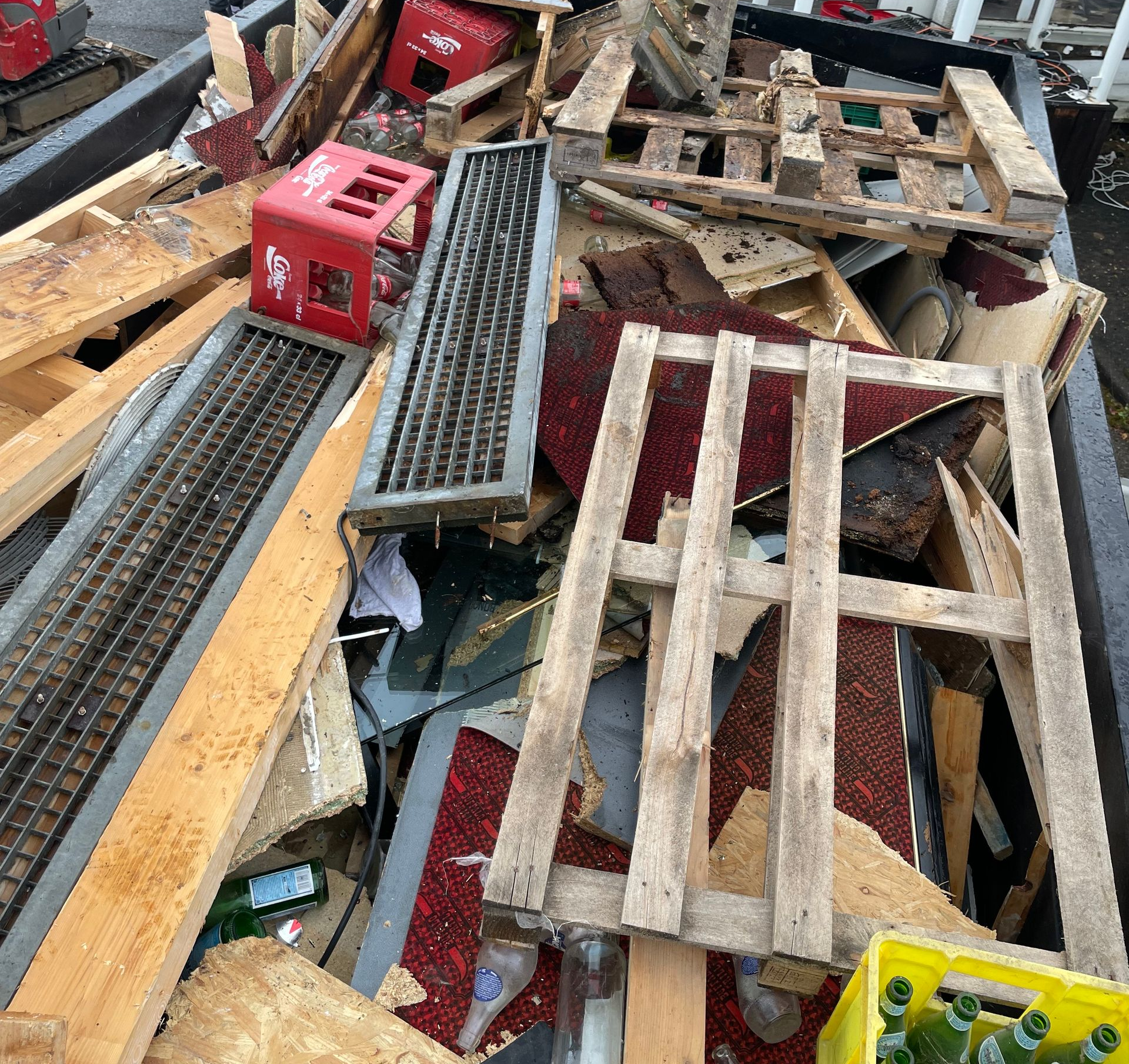 Un tas de bois, de palettes et de débris dans un conteneur métallique, comprenant une caisse rouge.