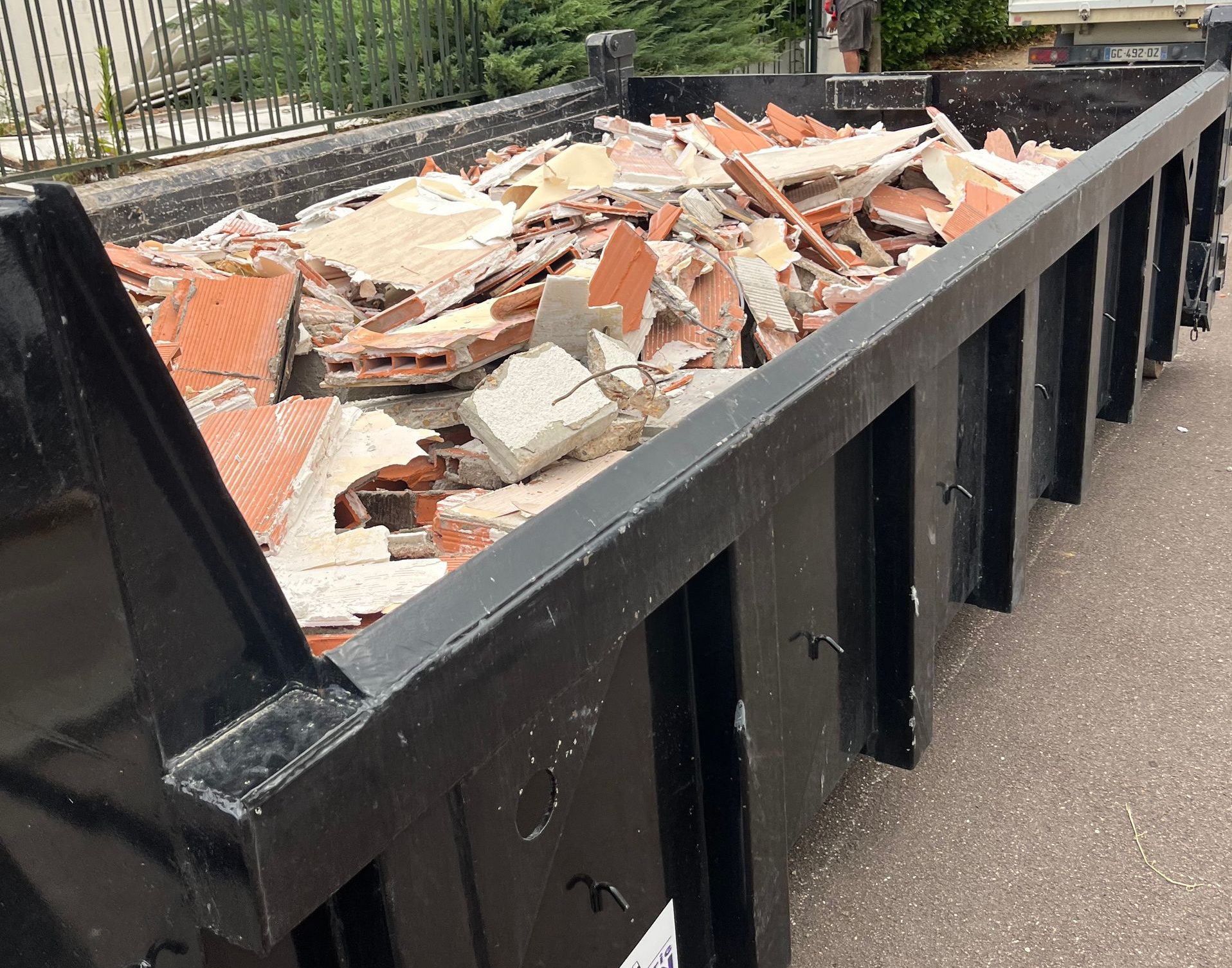 Benne noire remplie de débris de construction rouges et blancs.