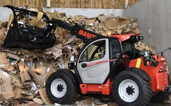 Un chariot élévateur orange soulève des déchets de carton compressé dans un entrepôt.