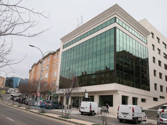 Un edificio con muchas ventanas y coches aparcados delante.