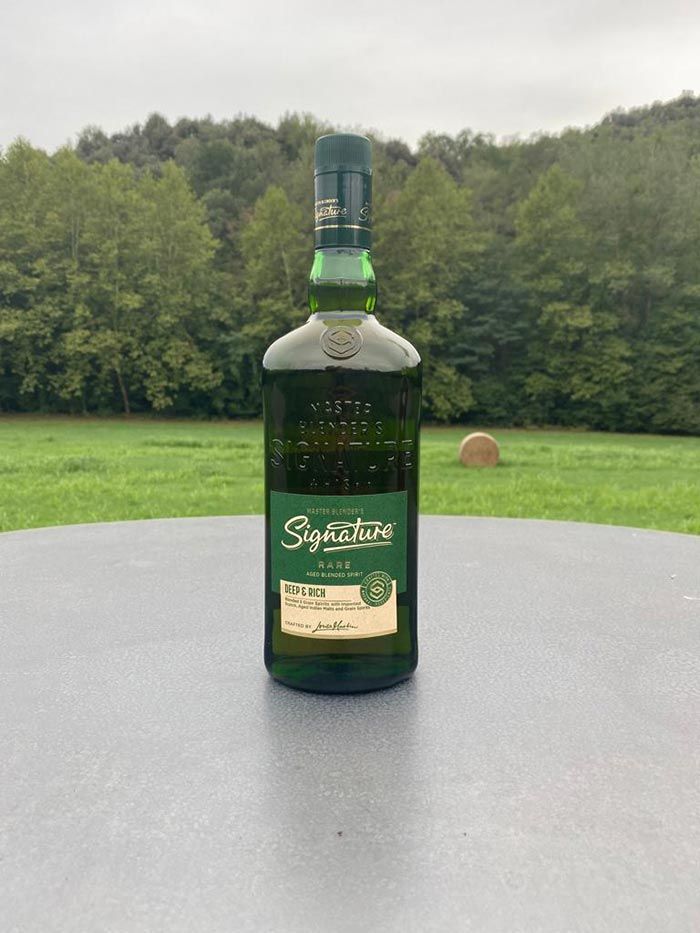 Una botella de whisky escocés está sobre una mesa frente a un campo.