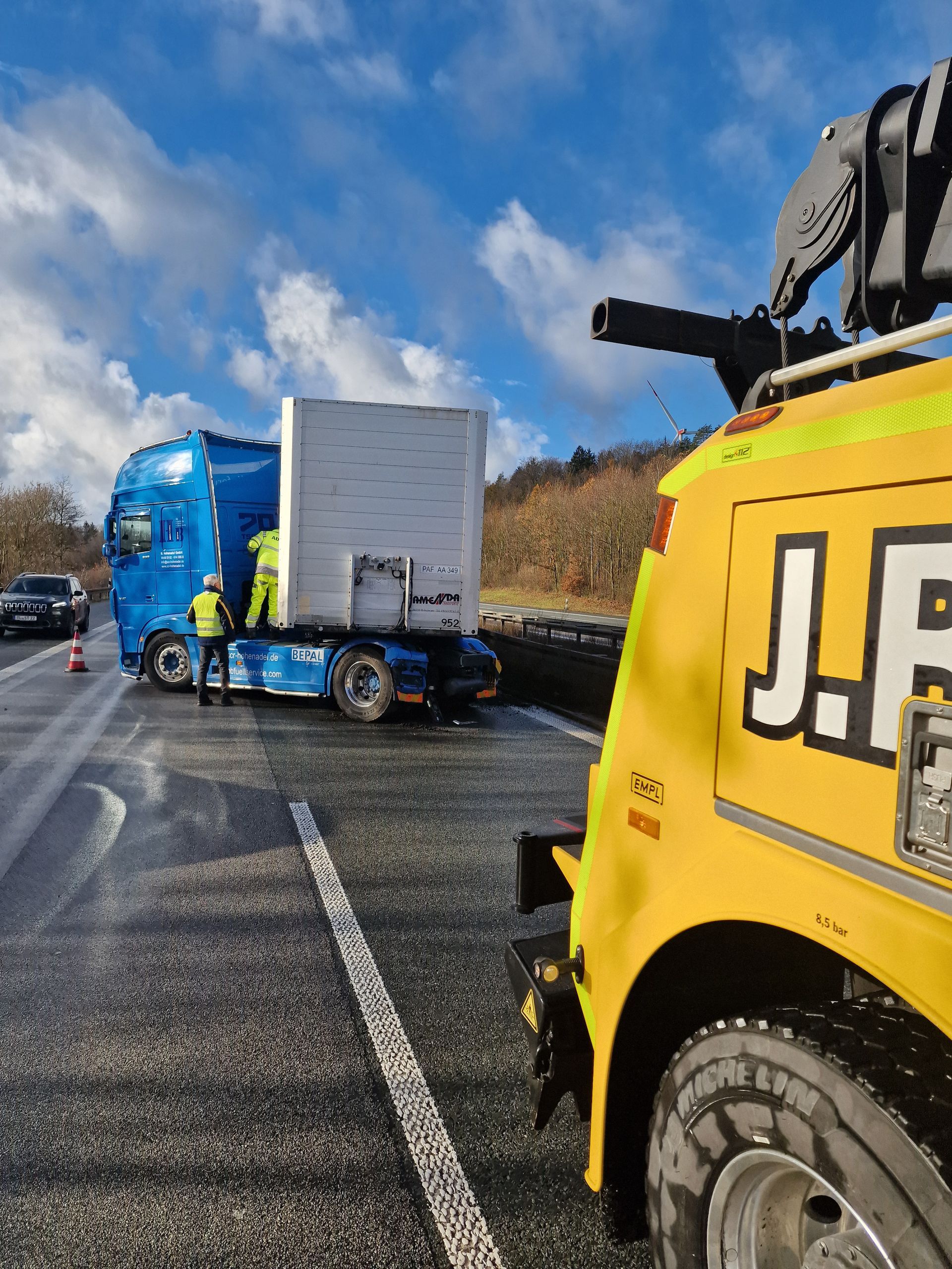 Ein blauer LKW wird von einem gelben Abschleppwagen mit der Aufschrift „jf“ abgeschleppt