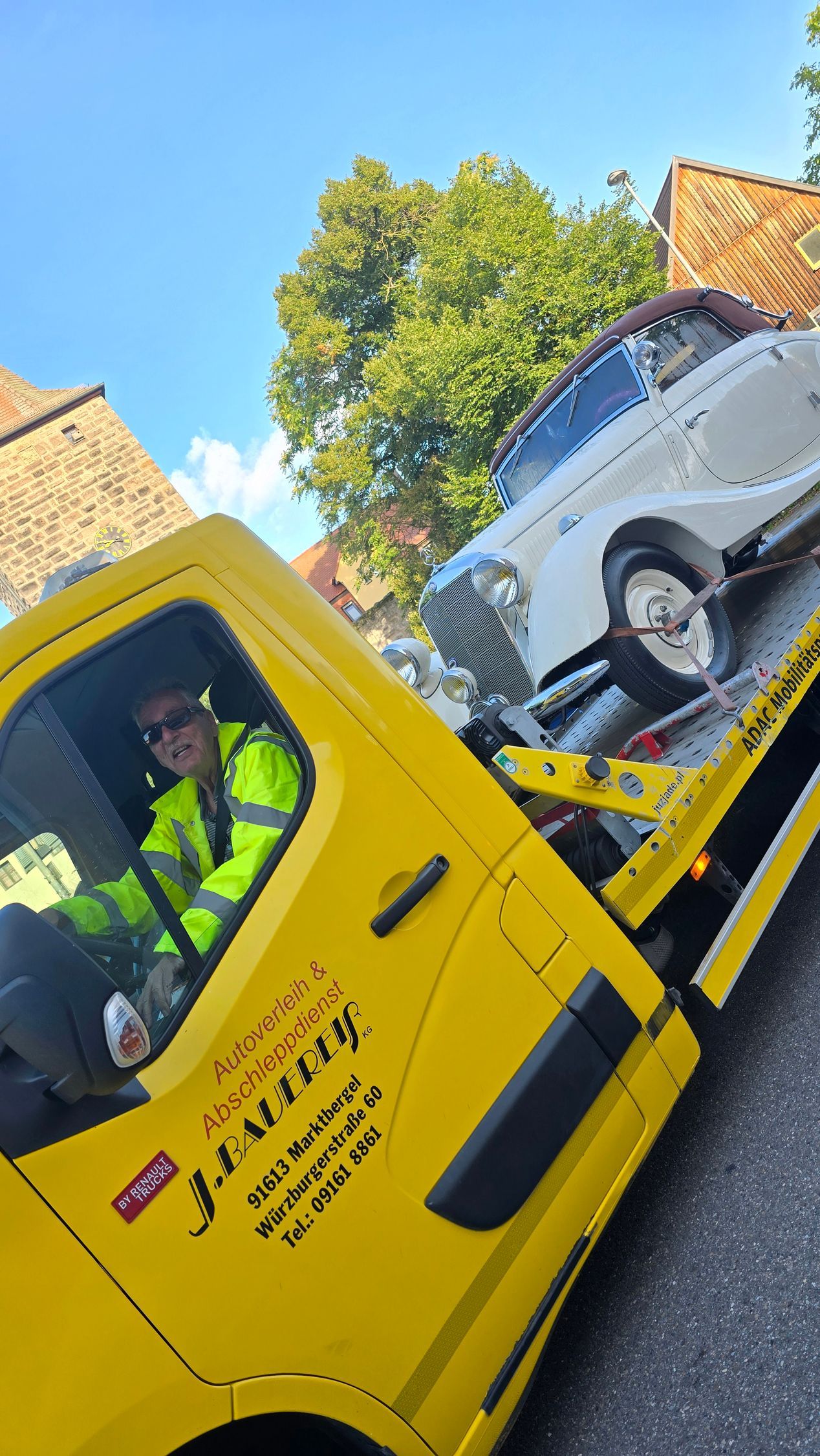 Ein Mann fährt einen gelben Abschleppwagen mit einem weißen Auto auf der Ladefläche.