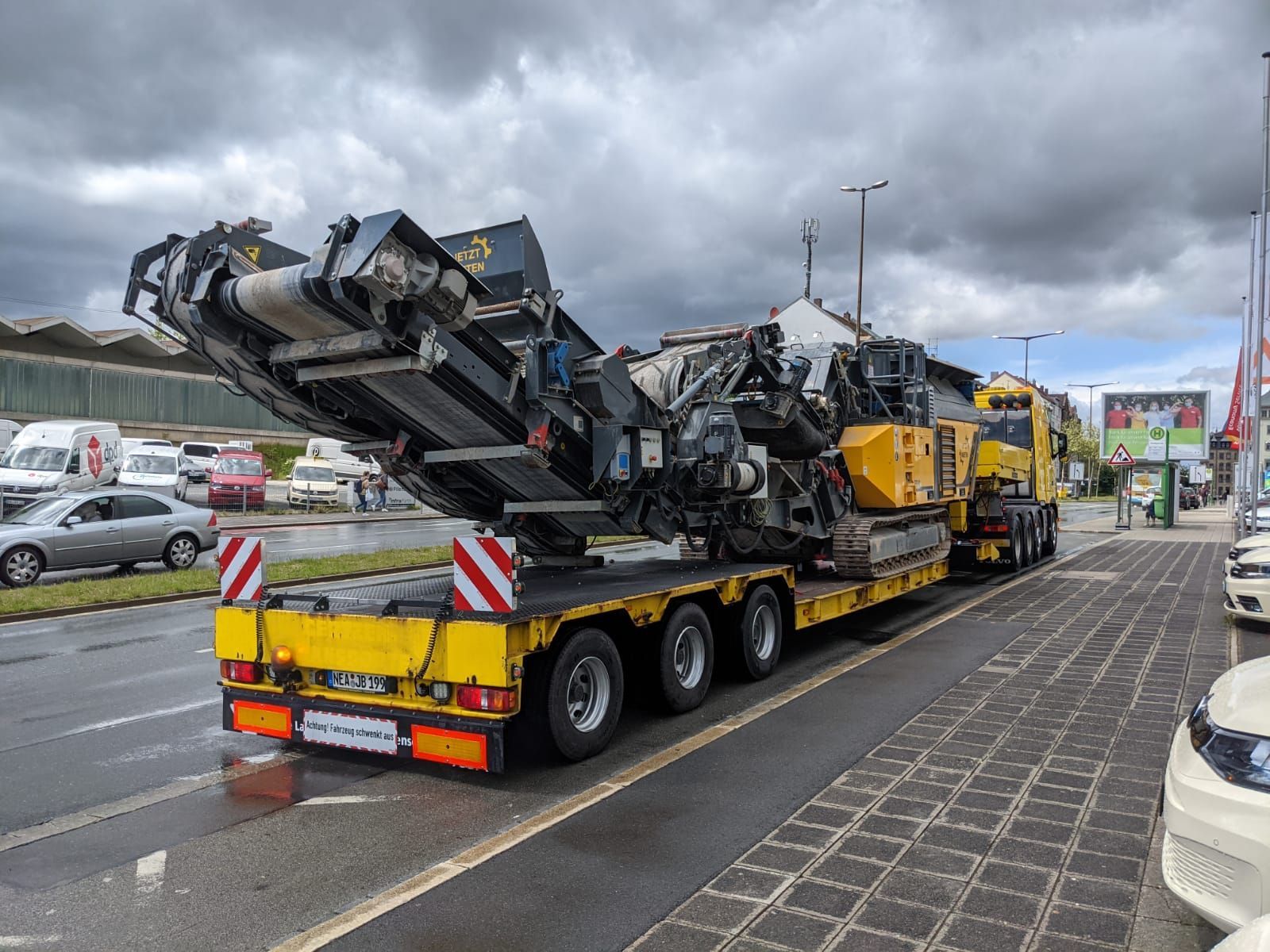 Ein gelber Lastwagen transportiert eine große Maschine auf einem Anhänger.