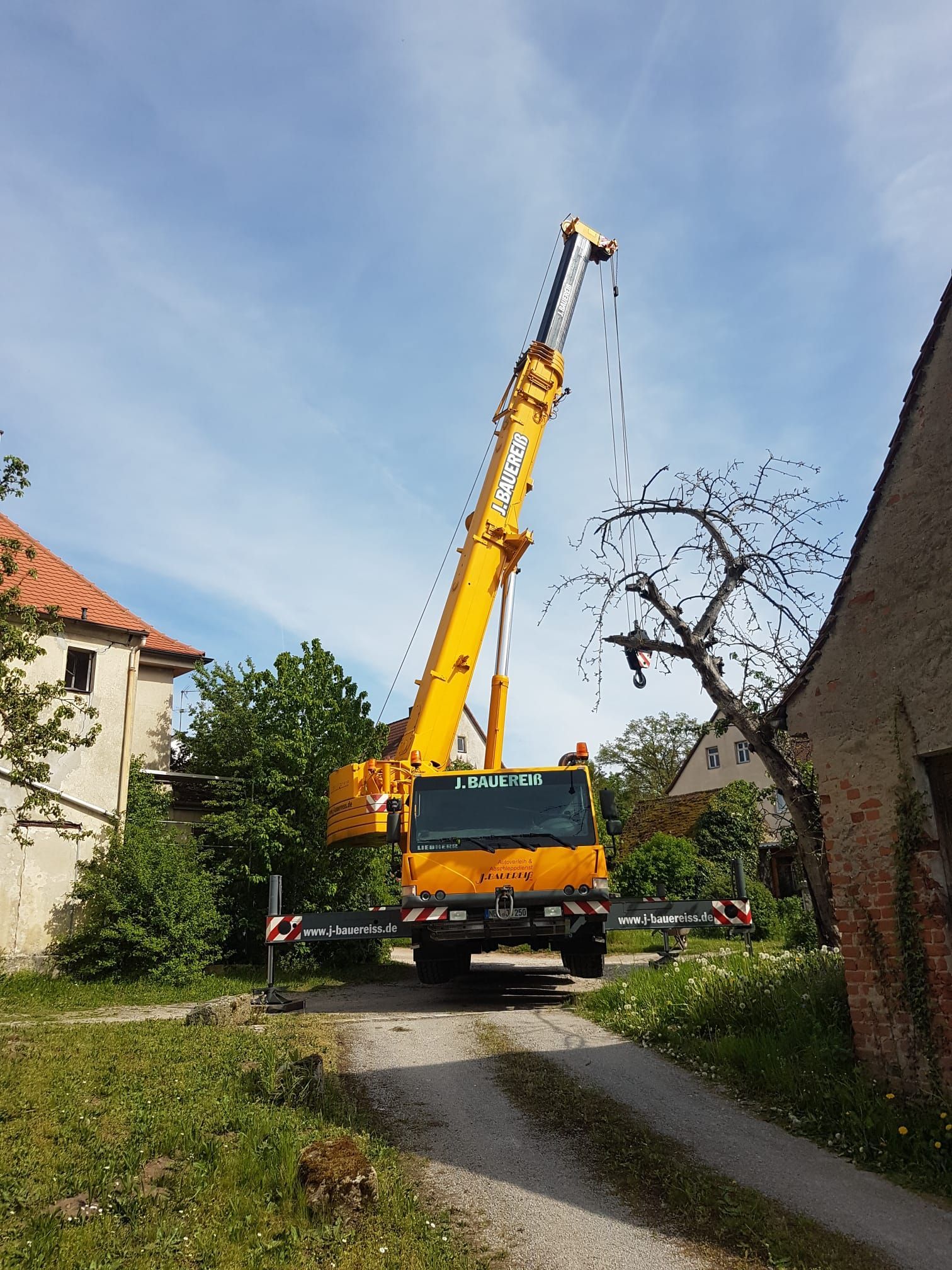 Ein großer gelber Kran steht am Rand einer unbefestigten Straße.
