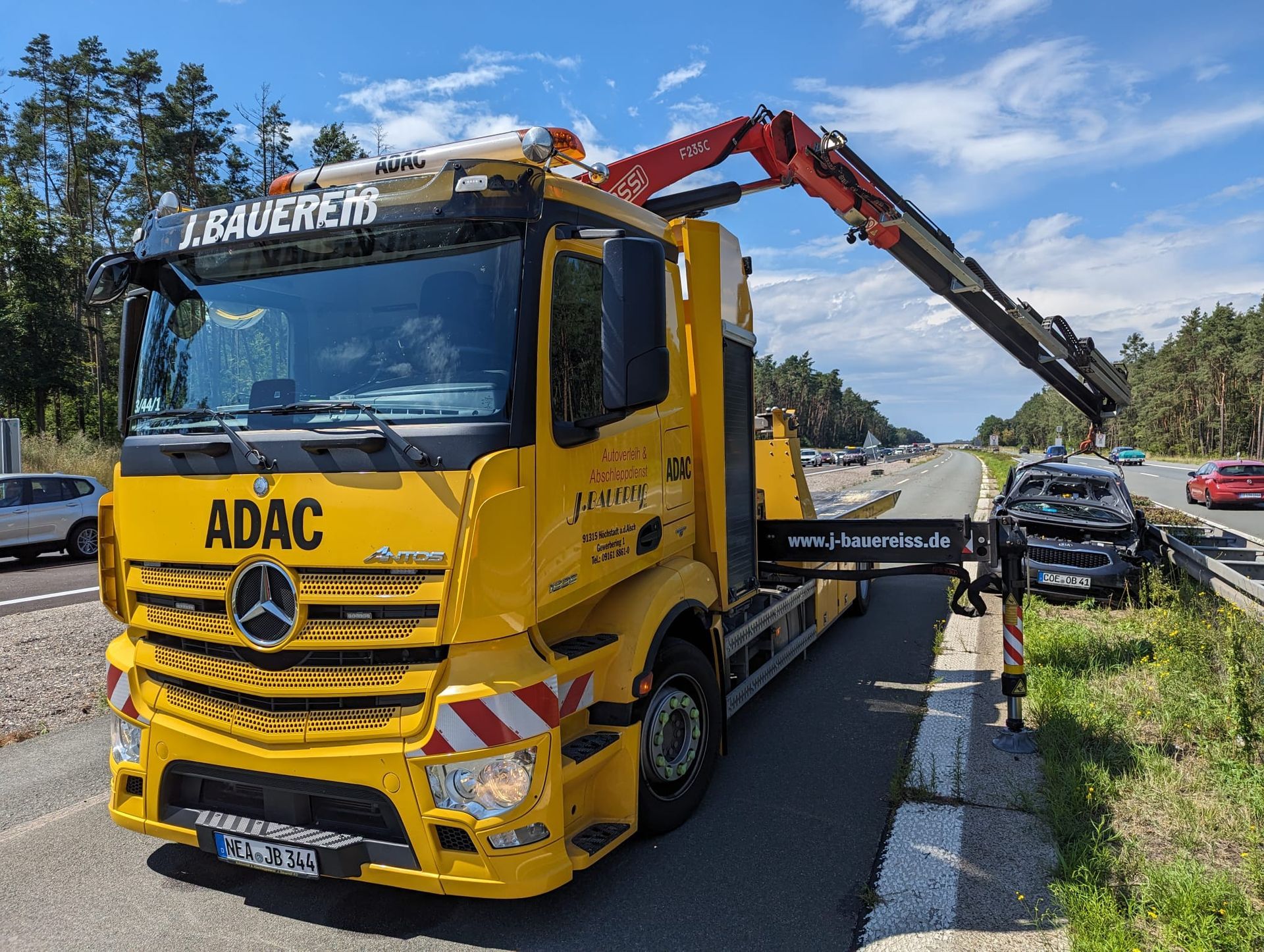 Ein gelber Lastwagen mit einem daran befestigten Kran steht am Straßenrand.
