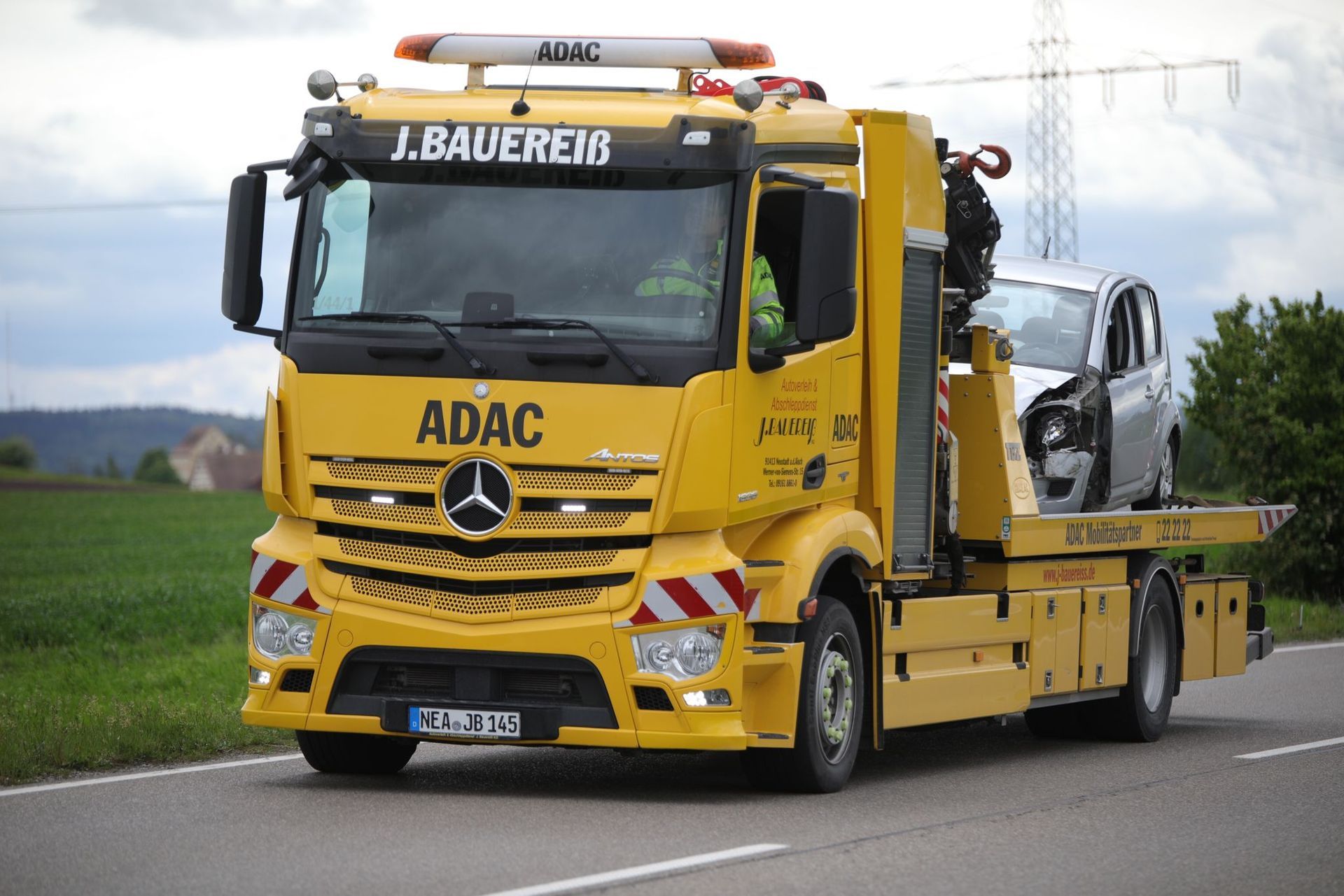 Ein gelber Abschleppwagen mit einem Auto auf der Ladefläche fährt eine Straße entlang.