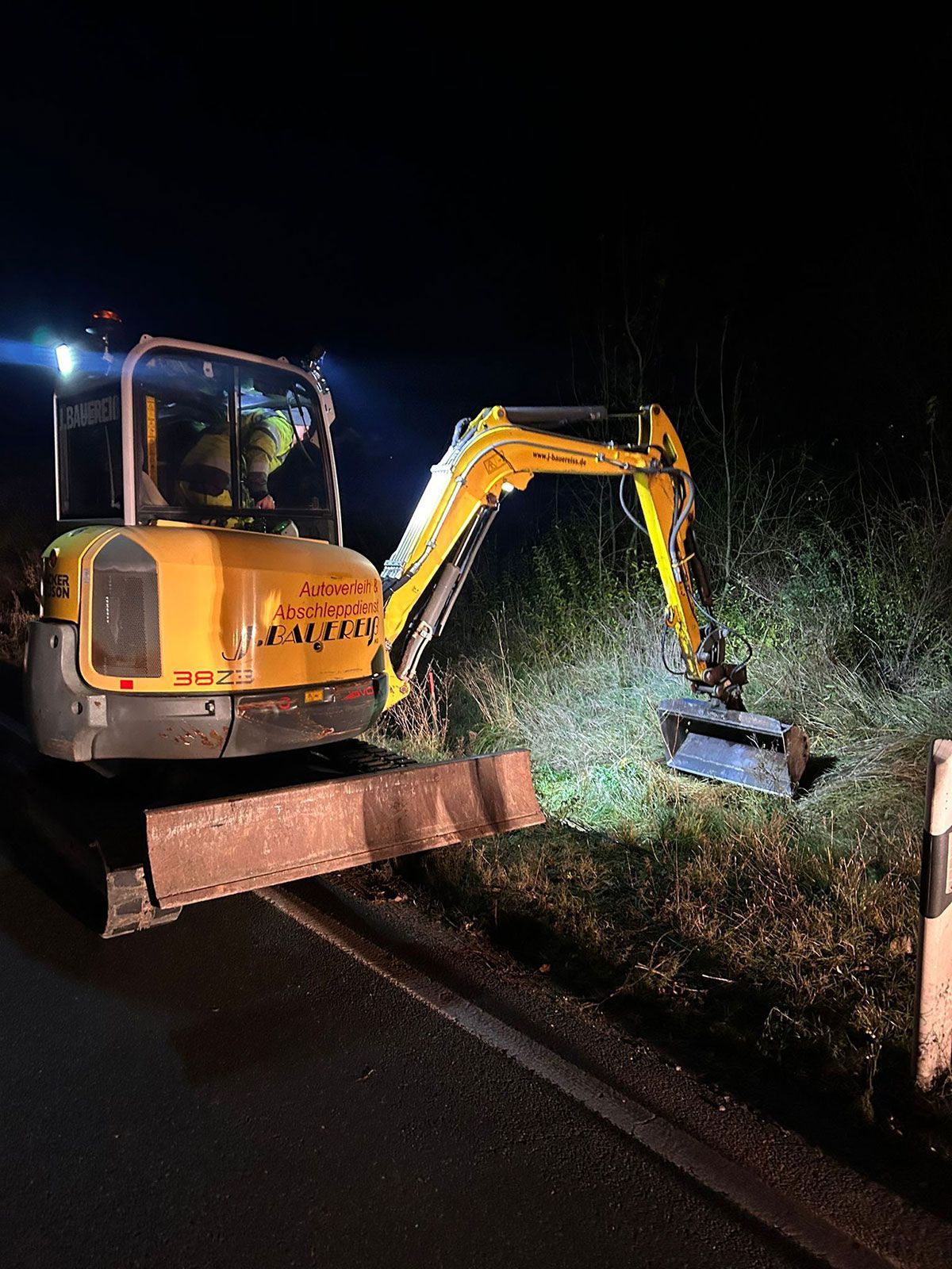 Ein gelber Bagger steht nachts am Straßenrand.